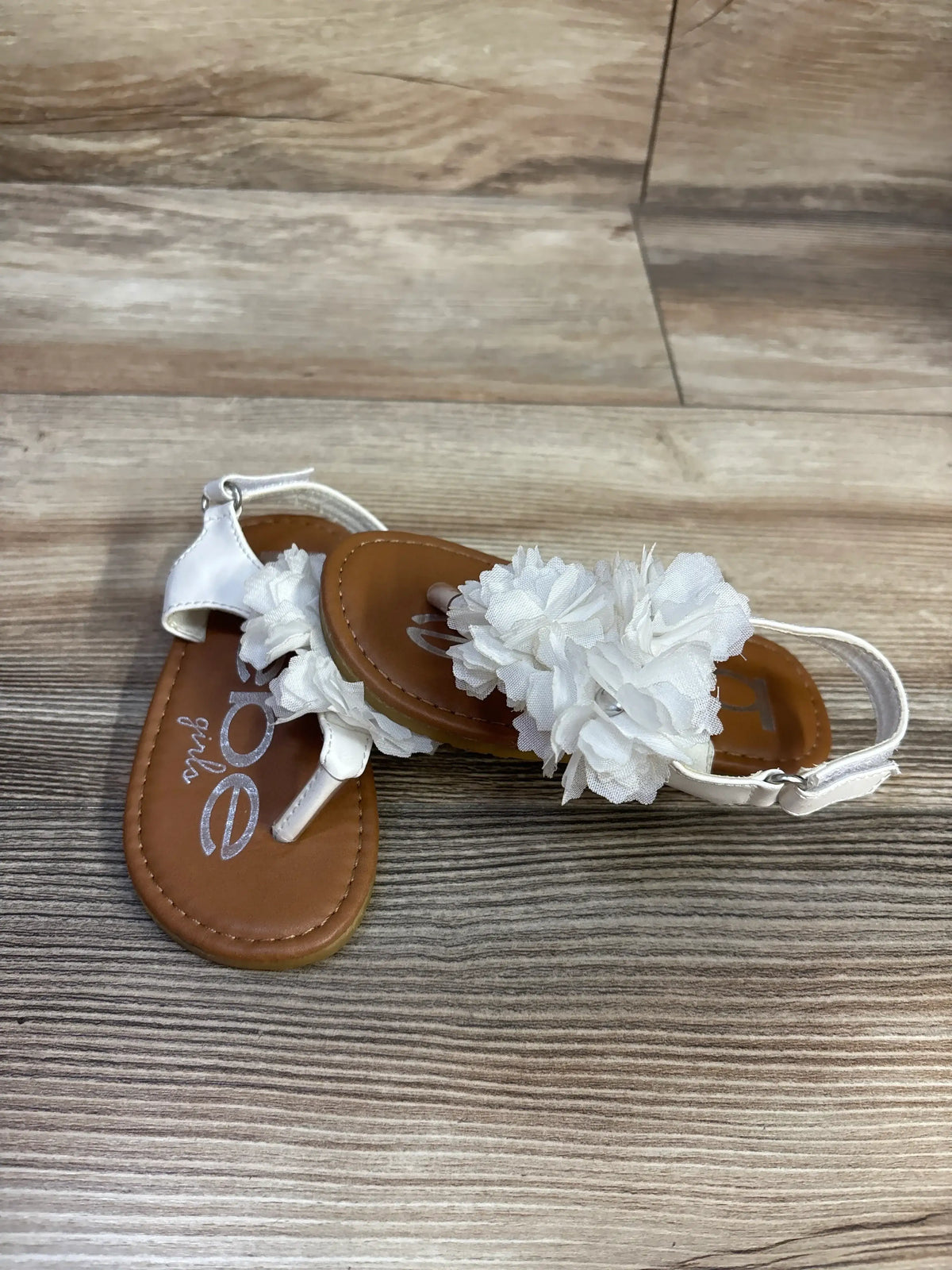 Top view of Bebe white chiffon flower sandals, size 7C, showcasing chiffon flower accents and ankle straps on wood-grain flooring