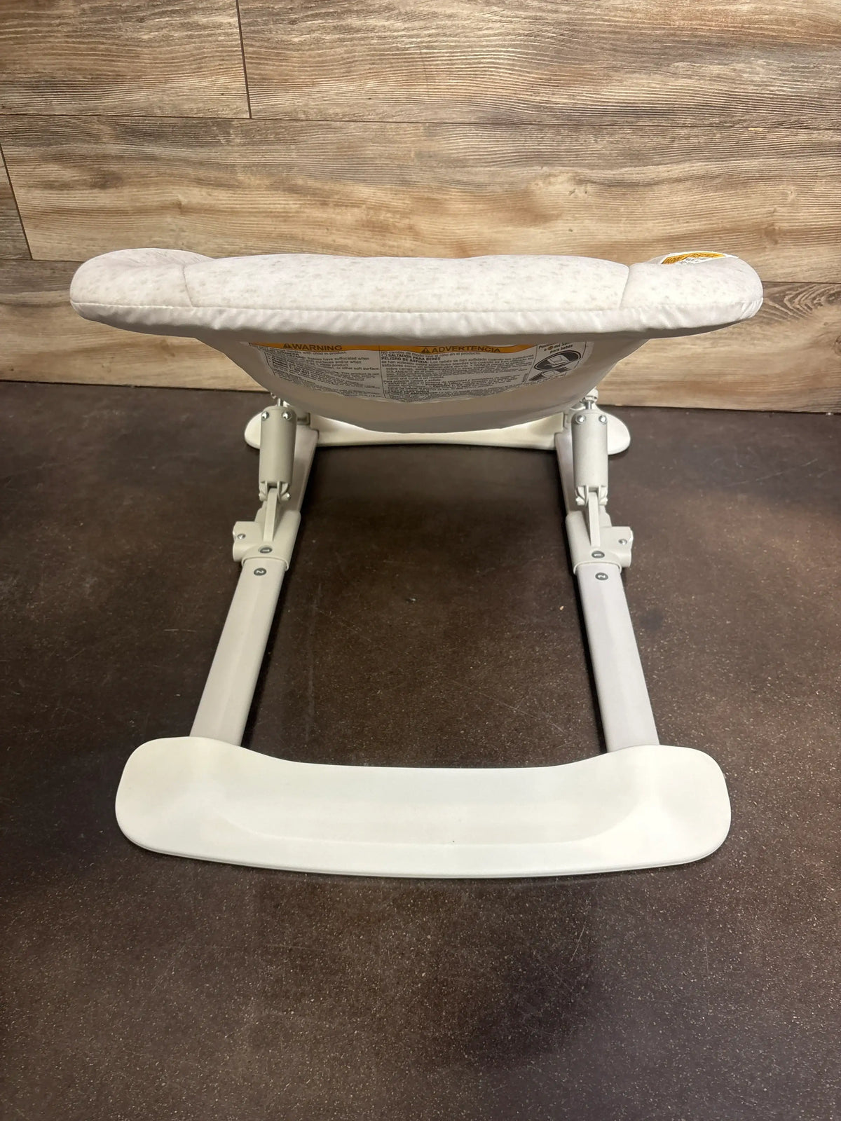 Rear view of Graco JumpStart 4-in-1 Activity Bouncer showcasing adjustable metal frame and white footrest on dark floor