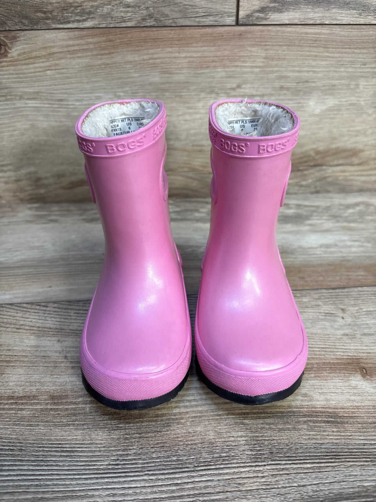 Front view of Bogs Skipper toddler pink rain boots showcasing faux-fur lining and black soles on wood background