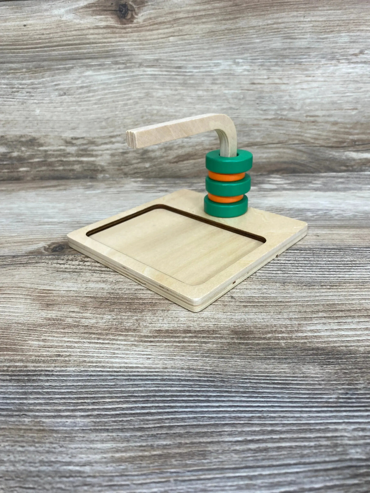 Three-quarter view of Monti Kids Curved Dowel showing curved wooden arm with green and orange stacking rings on a wood-grain background