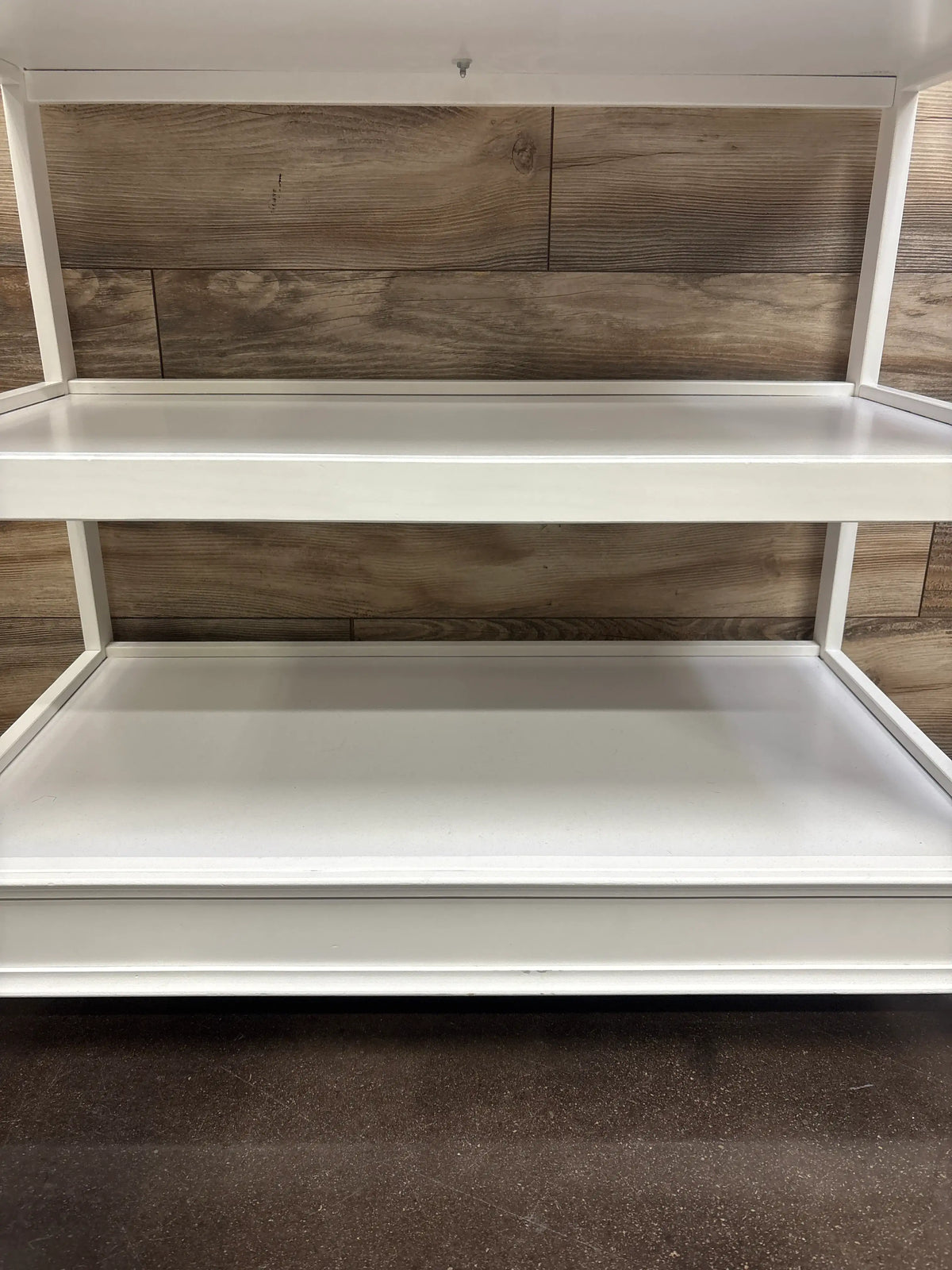 Front view of Delta Children Wilmington changing table showcasing two open shelves and white finish against a wood-paneled wall