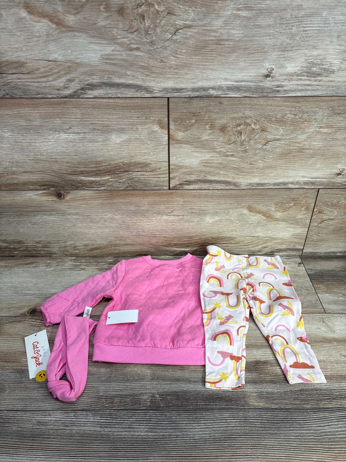 Pink baby sweatshirt, headband, and white leggings with rainbows and stars on wooden background
