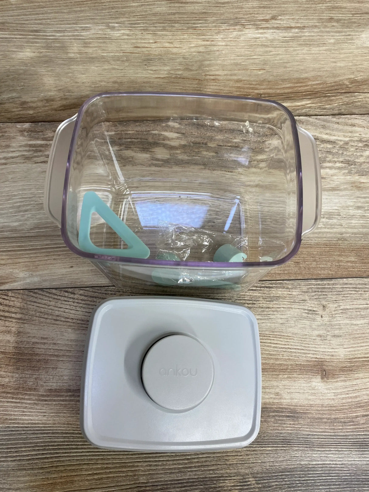 Top view of Ankou formula container with lid removed, clear square tub with purple rim, teal scoop, white lid embossed ankou
