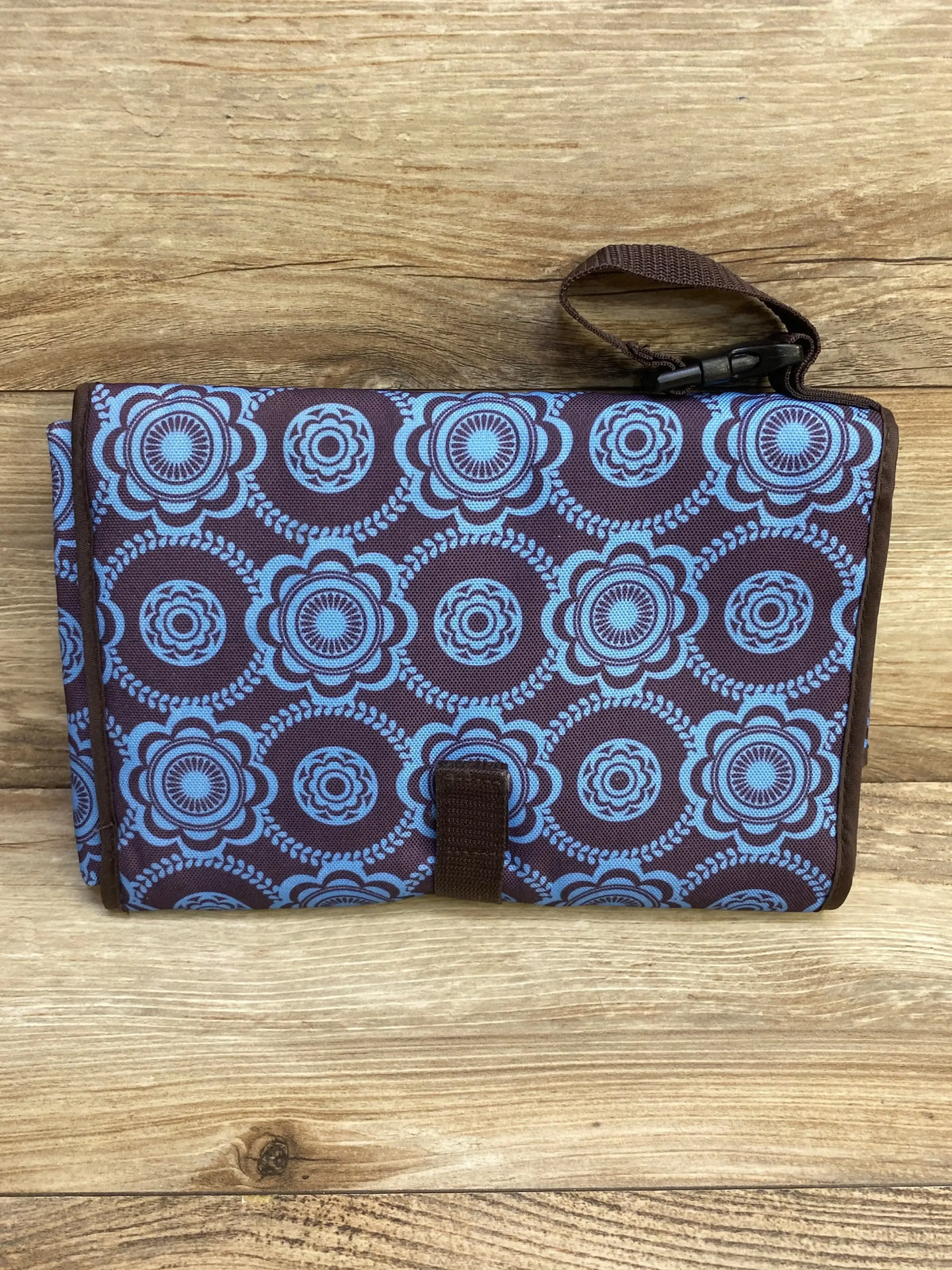Folded Avon Tiny Tillia changing pad with blue floral circles, wrist strap and snap closure on wood background