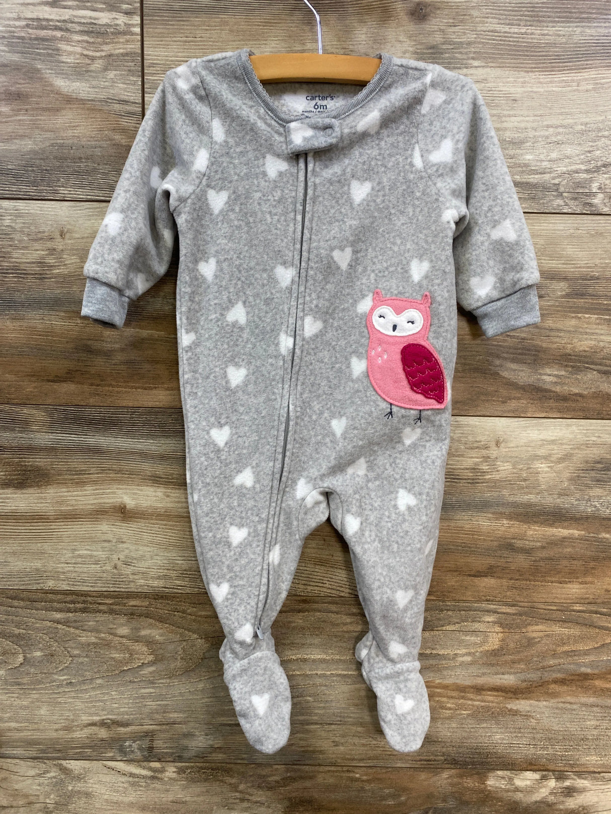 Gray baby sleeper with white hearts and pink owl patch, hanging on wooden background