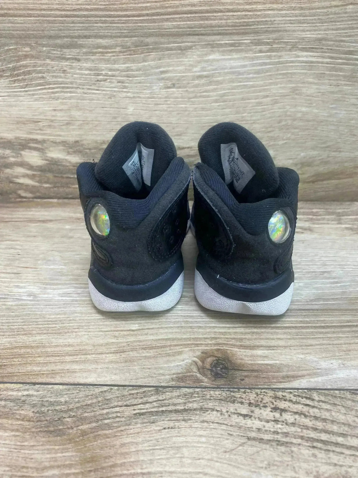 Rear view of toddler black Air Jordan 13 'Playoff' sneakers showing holographic heel pods and white midsoles on wood floor