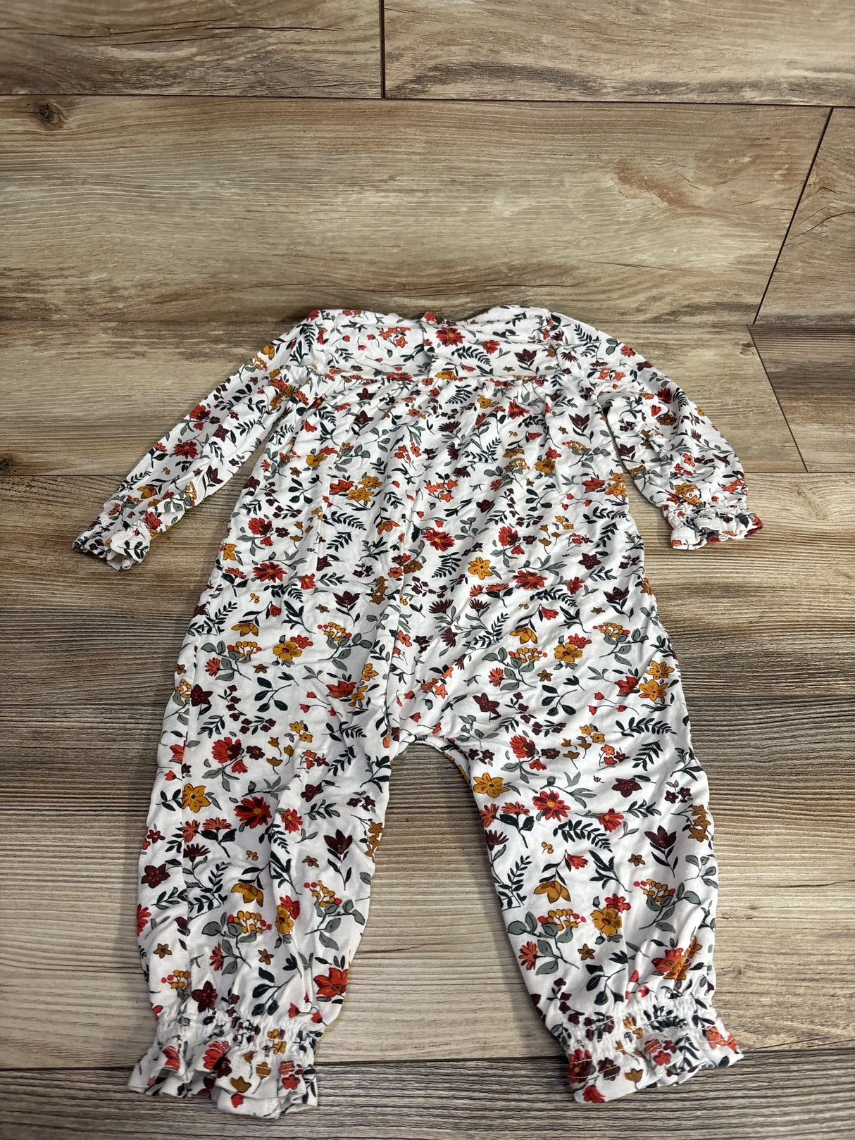Long sleeve baby romper with floral print, white background, laid on wood floor