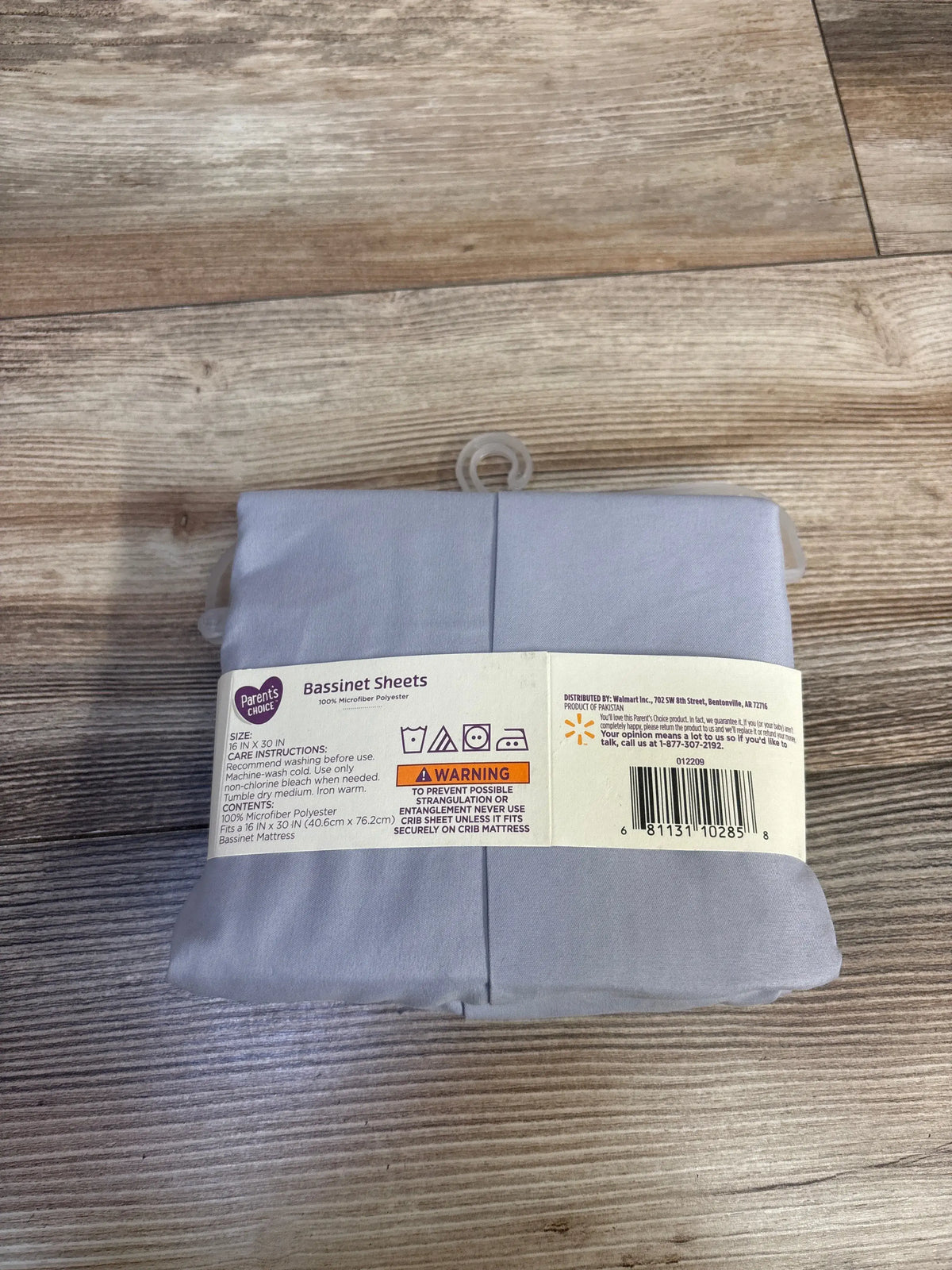 Overhead view of gray Parent’s Choice bassinet sheets, 2-count set, folded with packaging band on a wood floor