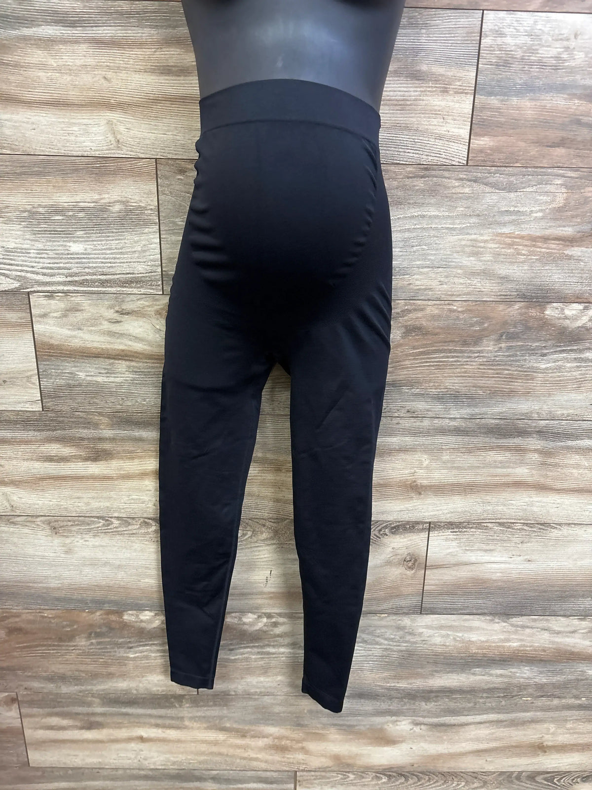 Front view of black maternity leggings with high over-belly support waistband on mannequin, wood background