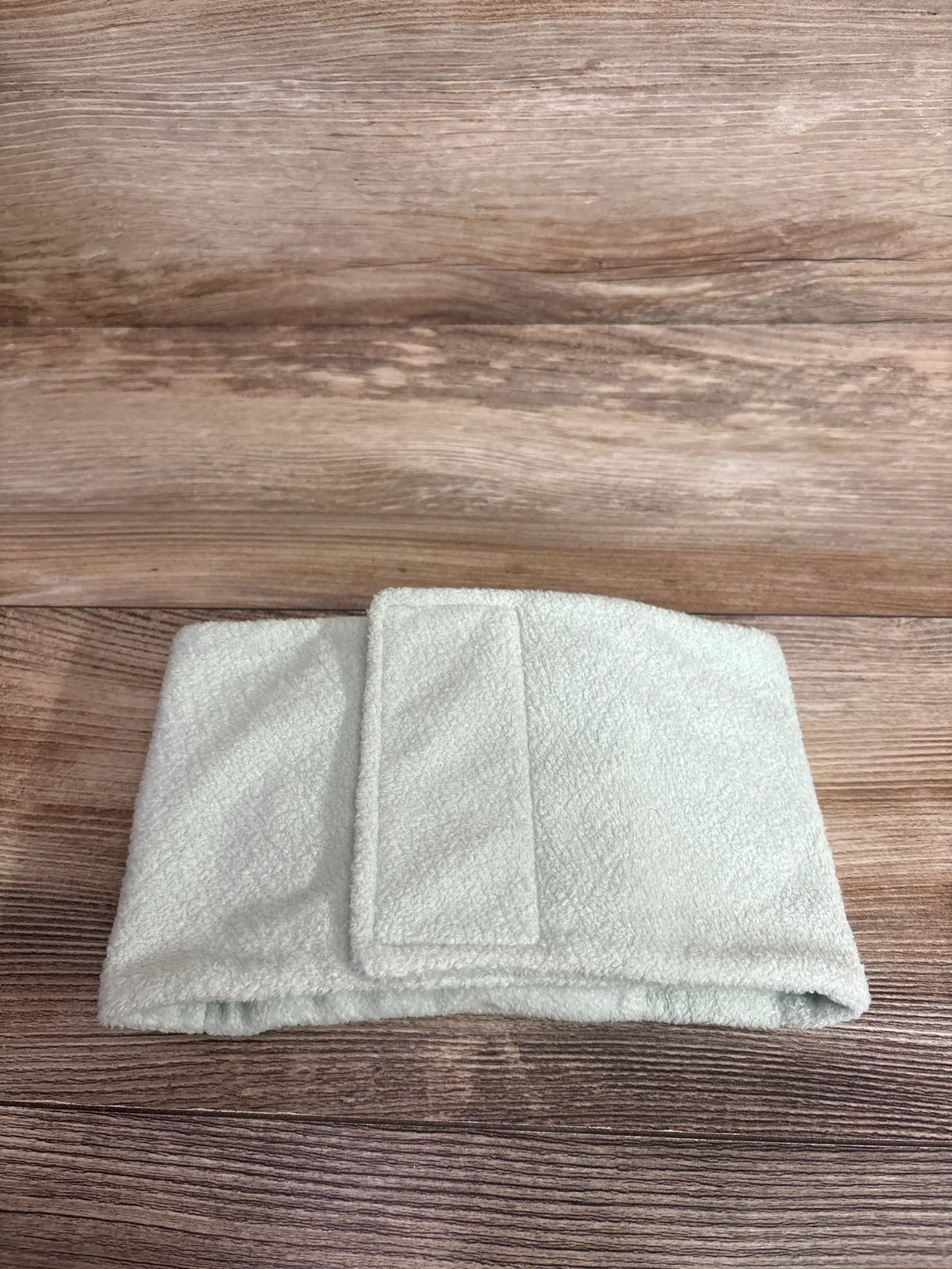 Folded front of Dr. Brown’s Infant GripeBelt showing Velcro closure, pale green with panda print on wood background