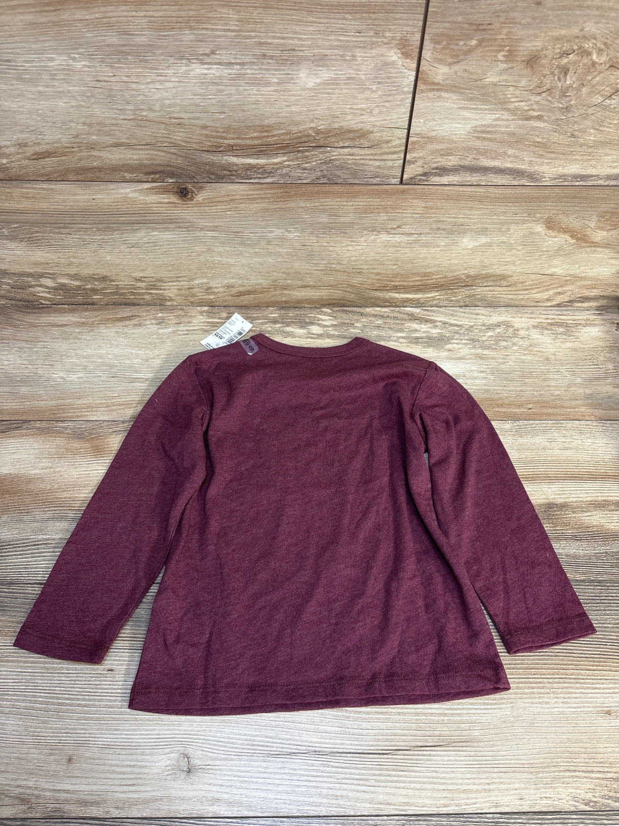 Burgundy long sleeve kids shirt laid flat on wood floor, resale clothing for children