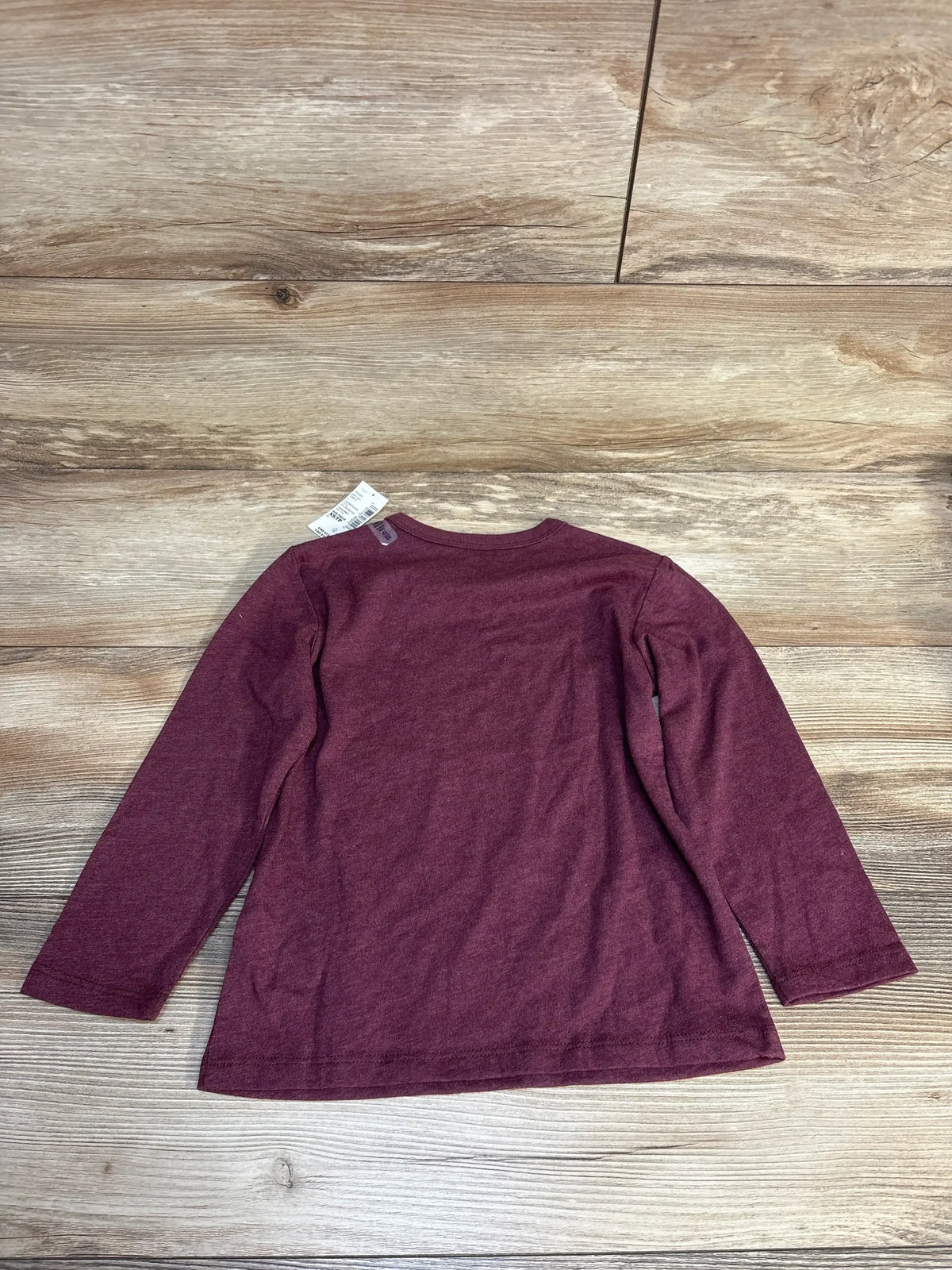 Burgundy long sleeve kids shirt laid flat on wood floor, resale clothing for children