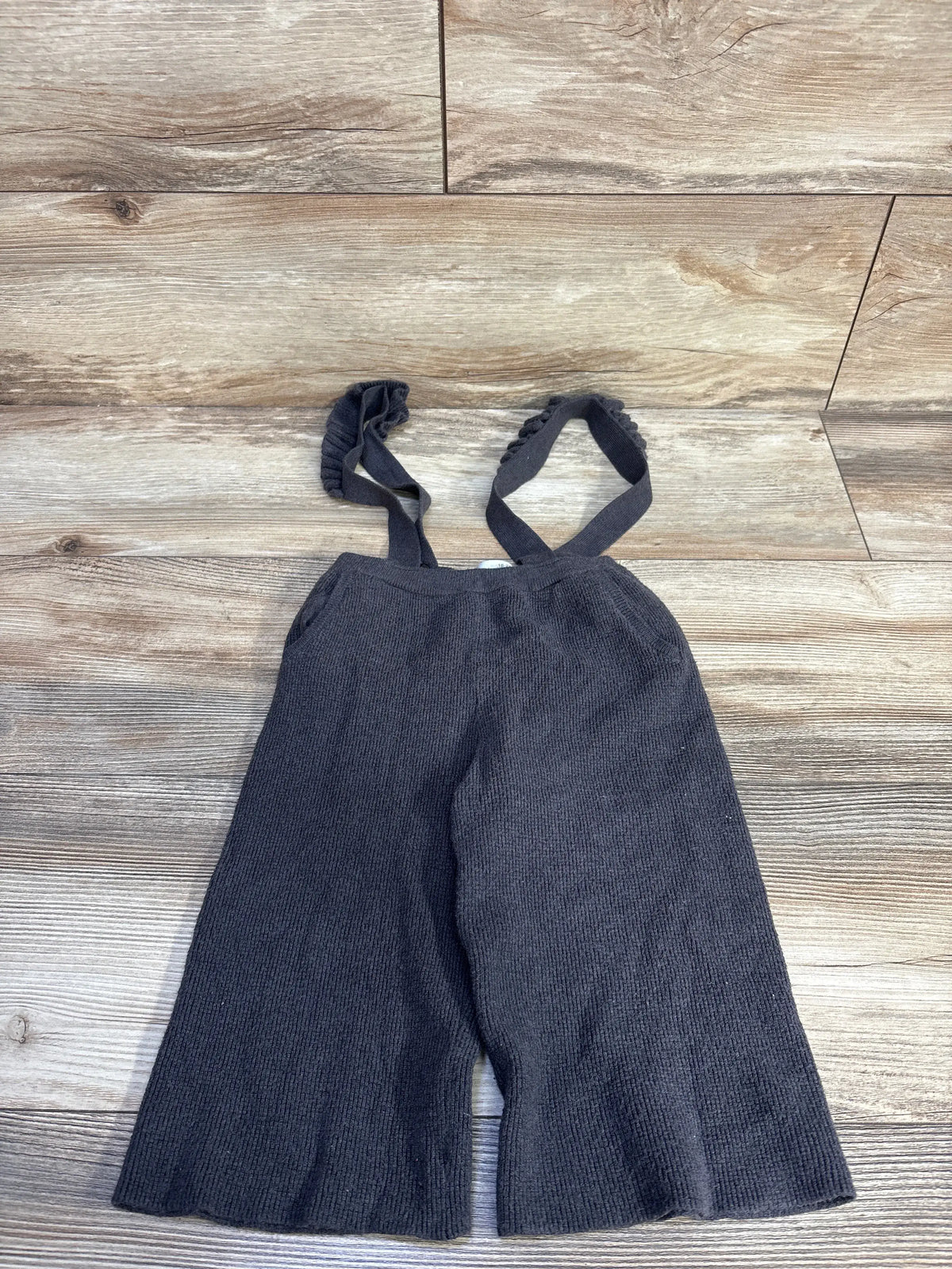 Flat lay of Zara knit suspender pants in grey, size 18-24 months, showcasing elastic waistband and straps on wood-look flooring