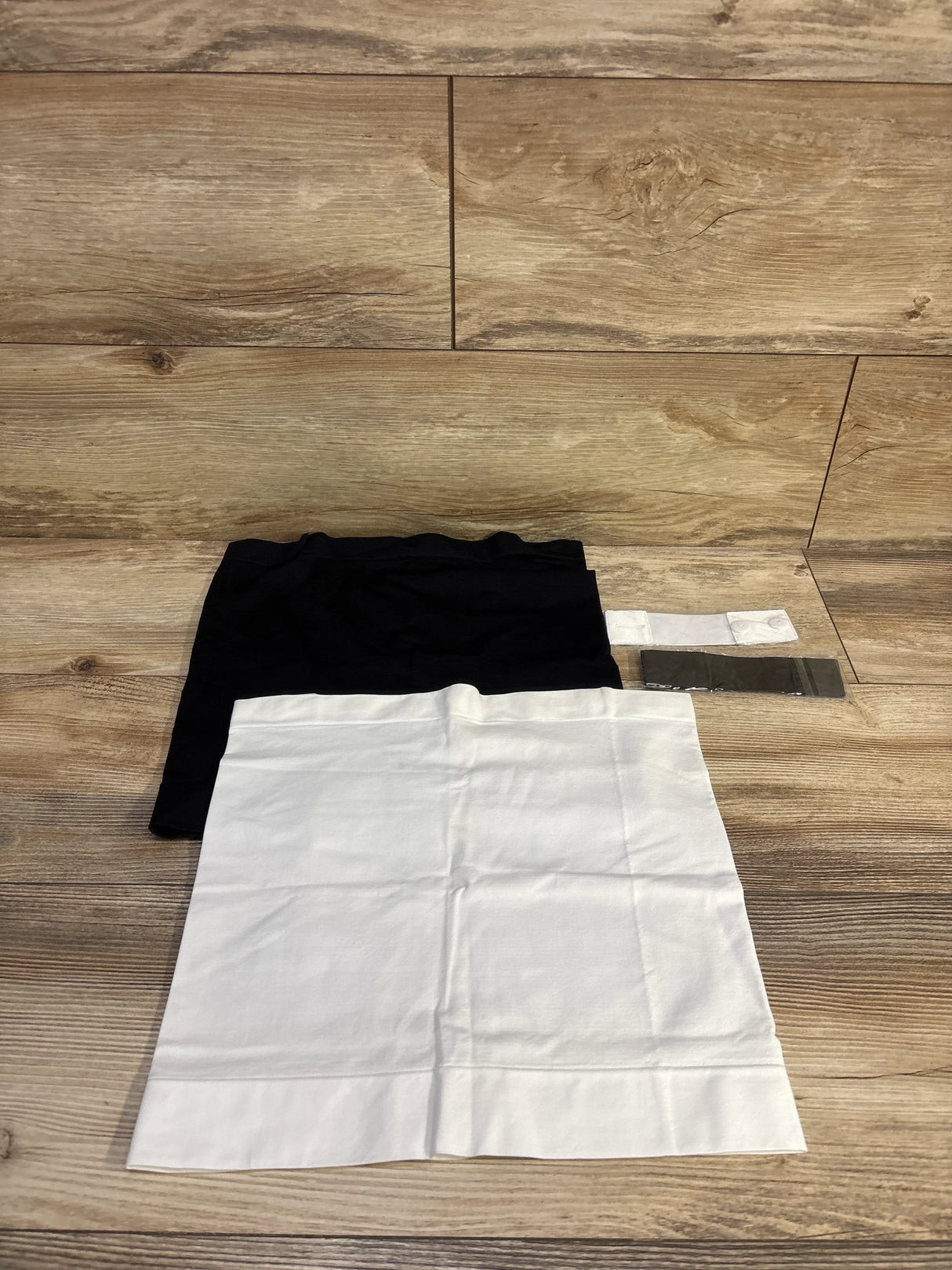 Top-down view of four-piece maternity waist extenders and belly bands in black and white laid flat on wood background showing stretch fabric and hook and eye extenders