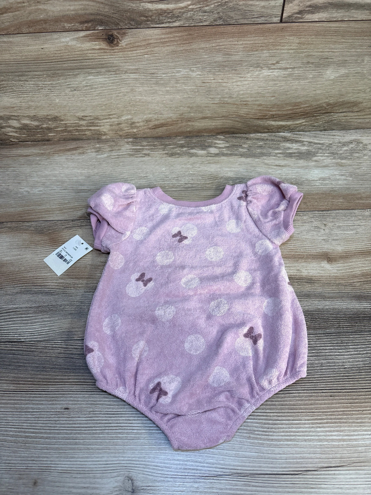 Flat lay of Disney Baby Minnie terry romper with puff sleeves and bow-and-polka-dot print on light pink fabric, wood background