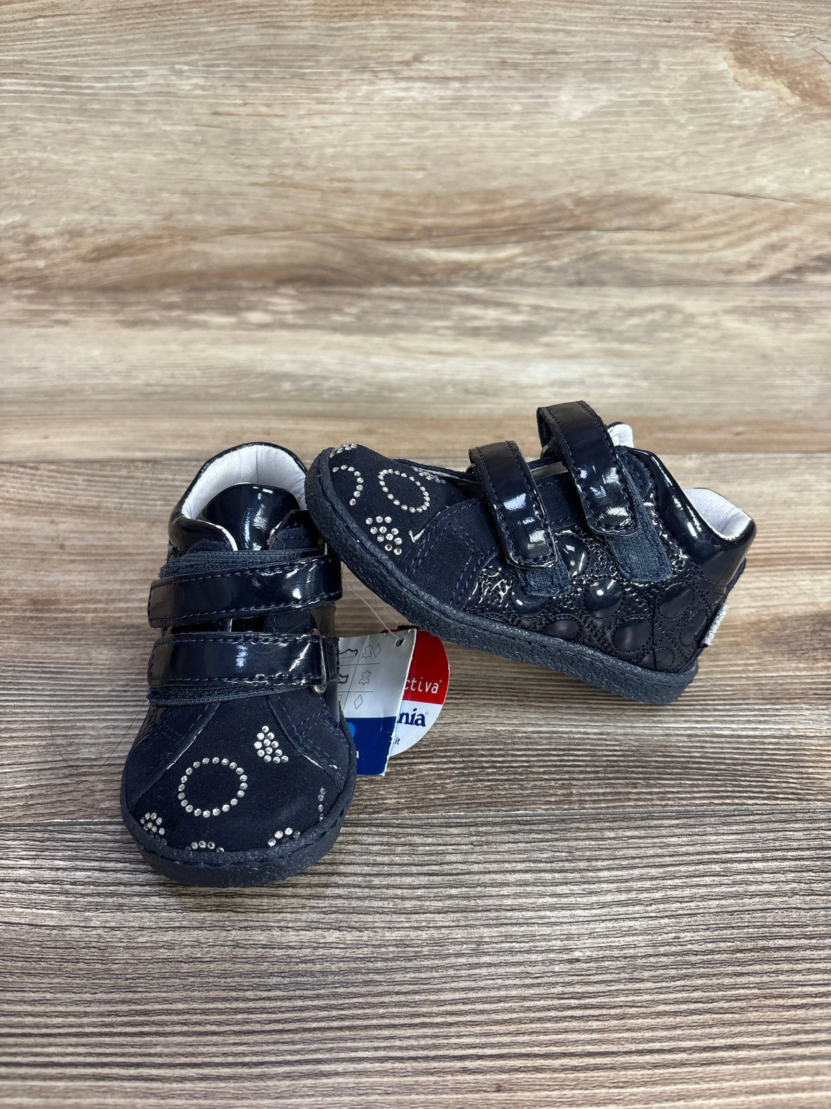 Pair of black baby shoes with velcro straps and silver studded circle designs on wooden background