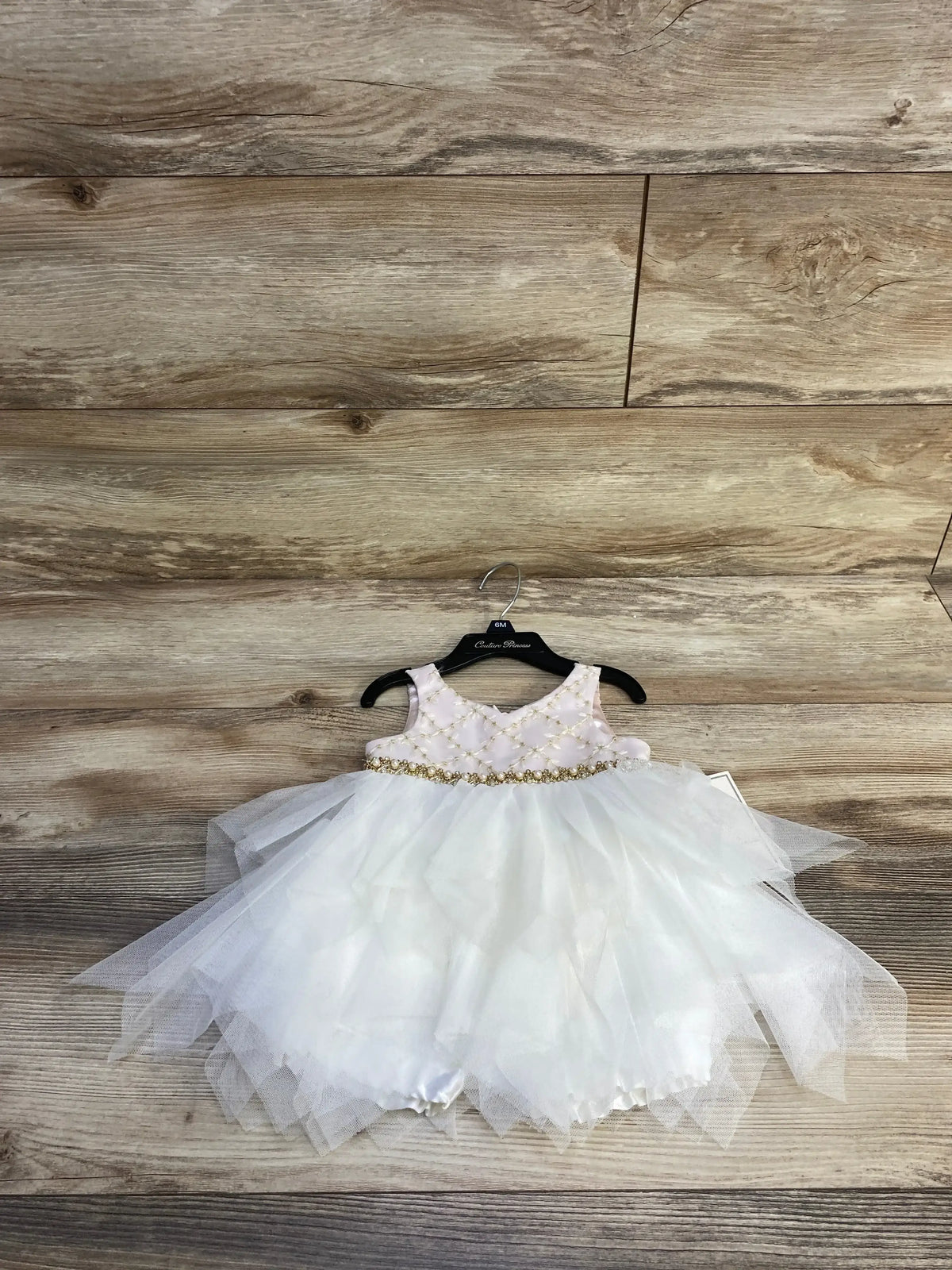 Front view of pink dress and bloomers with pearl-embroidered bodice, gold beaded waist and layered tulle skirt on wood background