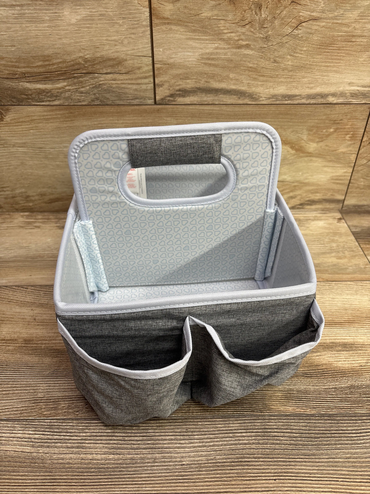 Front view of grey Munchkin portable diaper caddy showcasing two exterior pockets and open storage area on wood floor