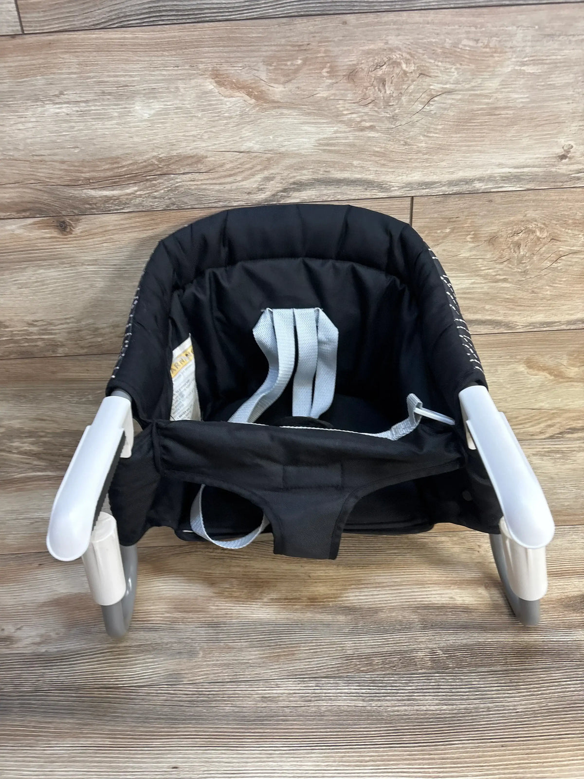 Black portable clip-on high chair with safety straps for babies, shown on wood floor