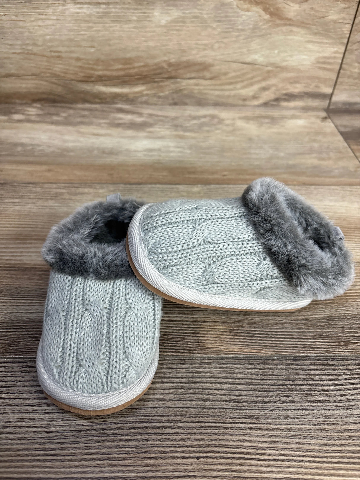 Gray toddler slippers with faux fur lining and knitted cable design on wood background
