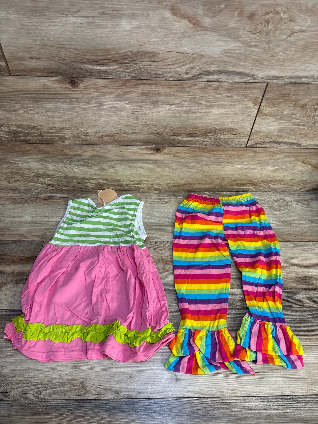 Girls' pink ruffle dress with green stripes and rainbow striped ruffle pants on wood floor