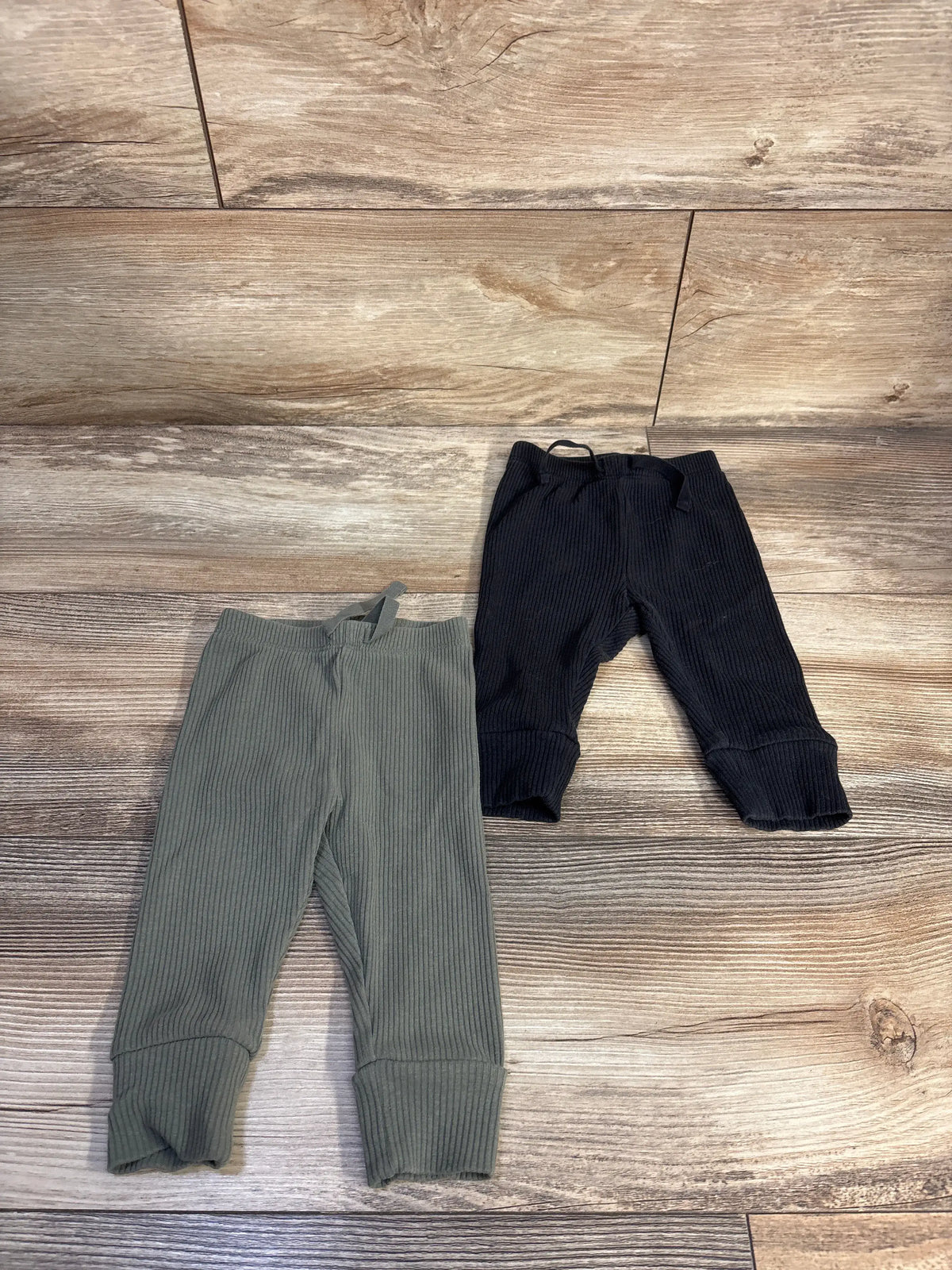 Top-down view of Baby Gap black ribbed pull-on pants two-pack with elastic waists and cuffed legs on a wood-look floor