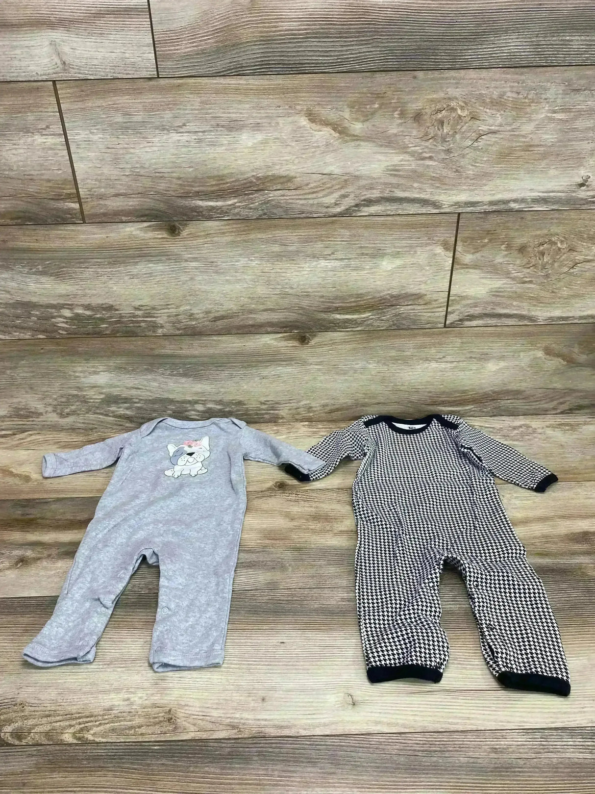 Two baby coveralls flat lay: gray coverall with dog applique and black-and-white patterned piece with navy trim on wood floor