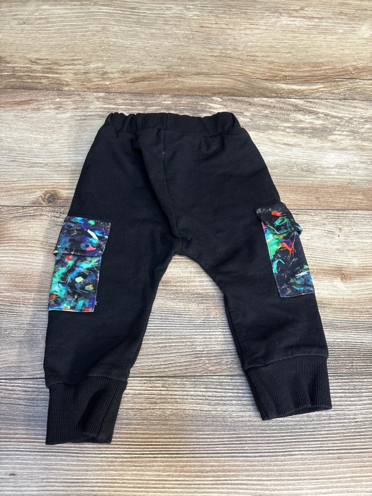 Black baby pants with colorful side pockets and ribbed cuffs on wooden background