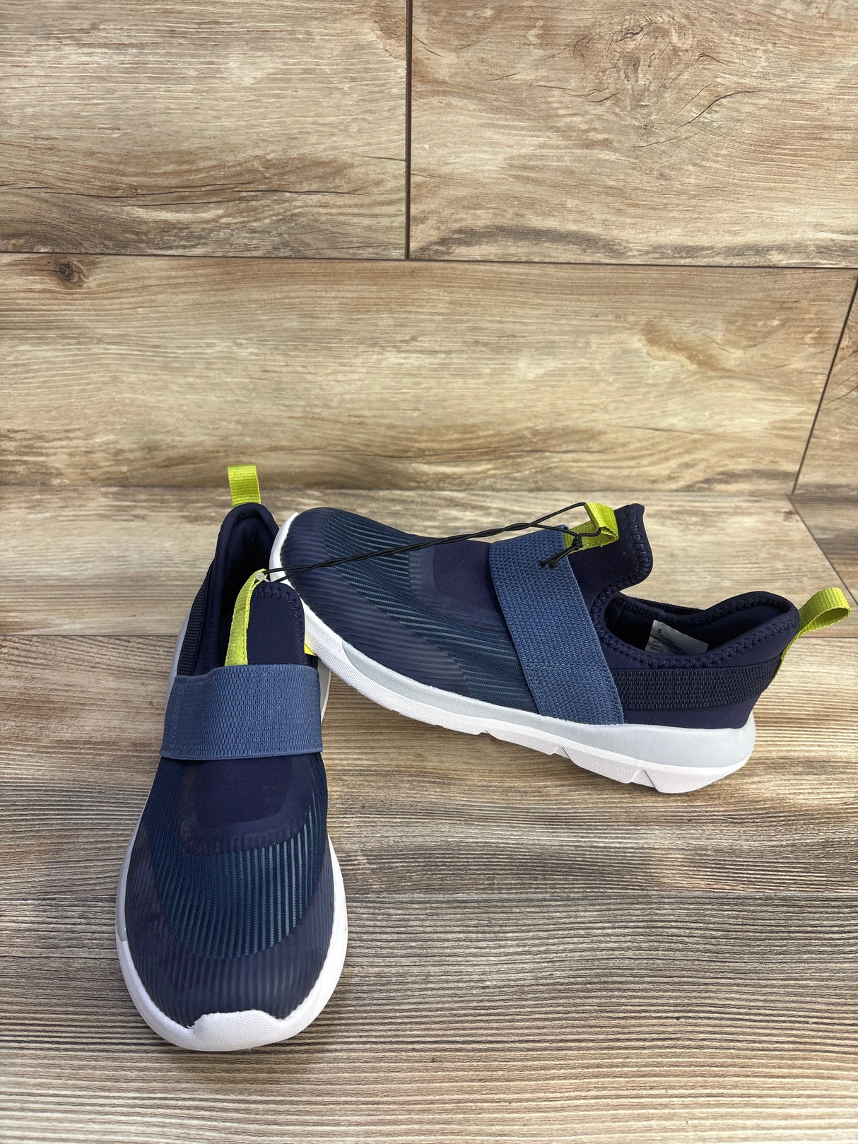 Front and side view of All In Motion kids navy slip-on sneaker showcasing elastic strap and white sole on wood background