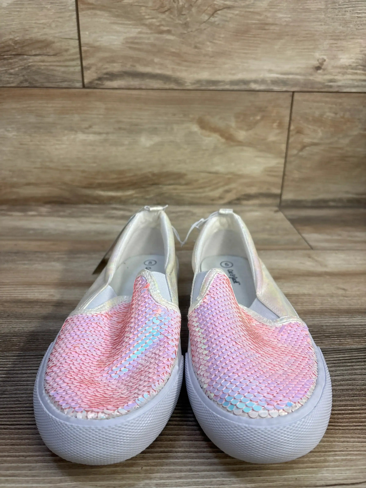 Front view of Cat & Jack Aliki slip-on sneakers with pink iridescent sequined uppers, white soles, and wood floor