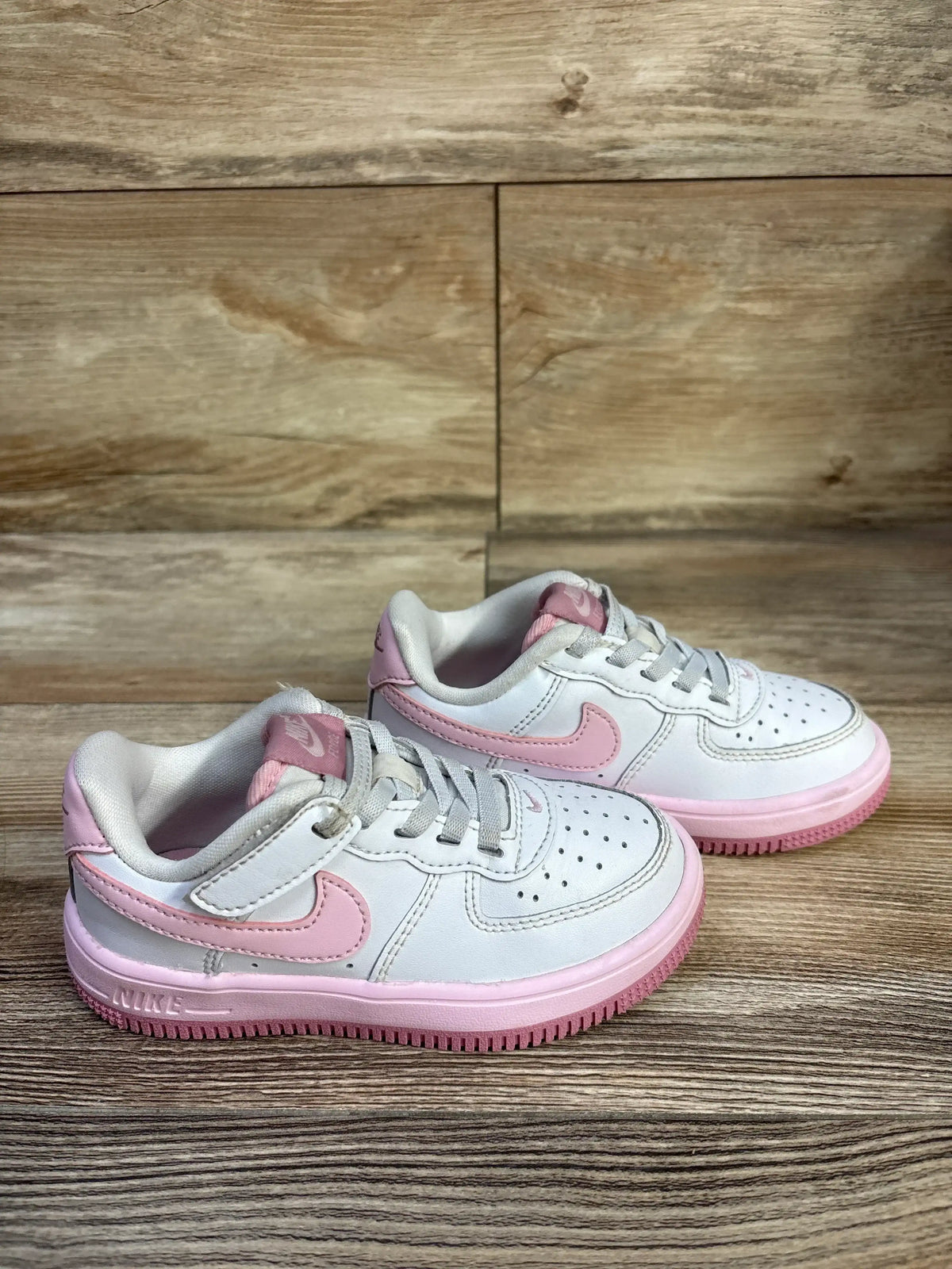 Side-angle view of toddler Nike Air Force 1 Low EasyOn sneaker showcasing white leather upper with pink swoosh and pink midsole on wood floor background