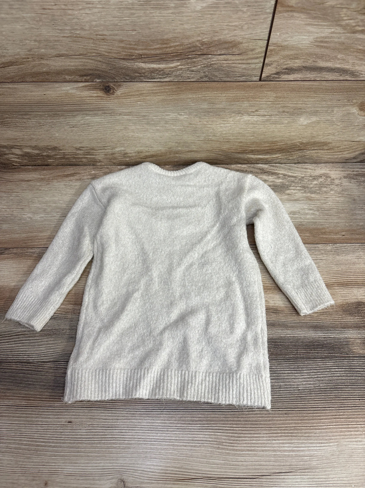 White long-sleeve knit sweater for kids laid flat on wooden floor