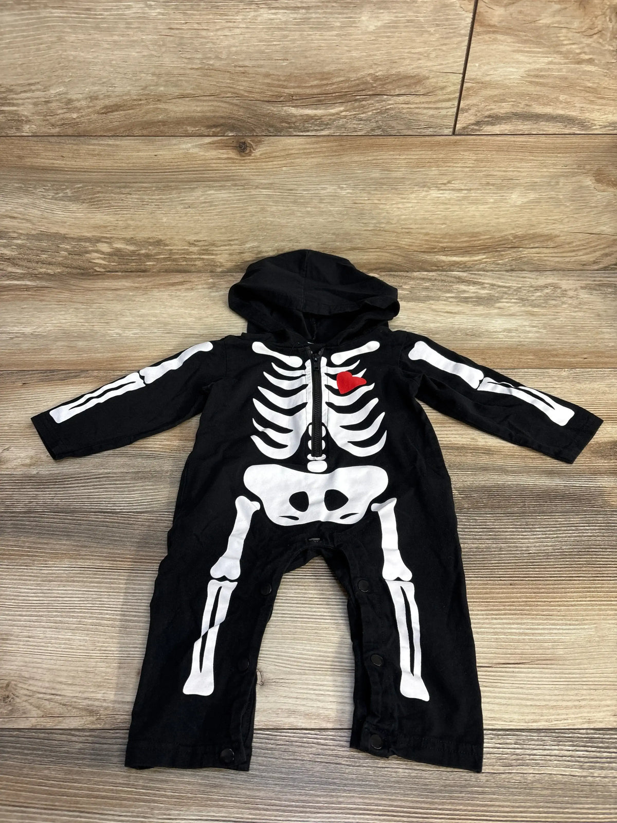 Flat lay of black baby hooded coverall (3-6 months) showcasing white skeleton print and red heart on chest with light wood background