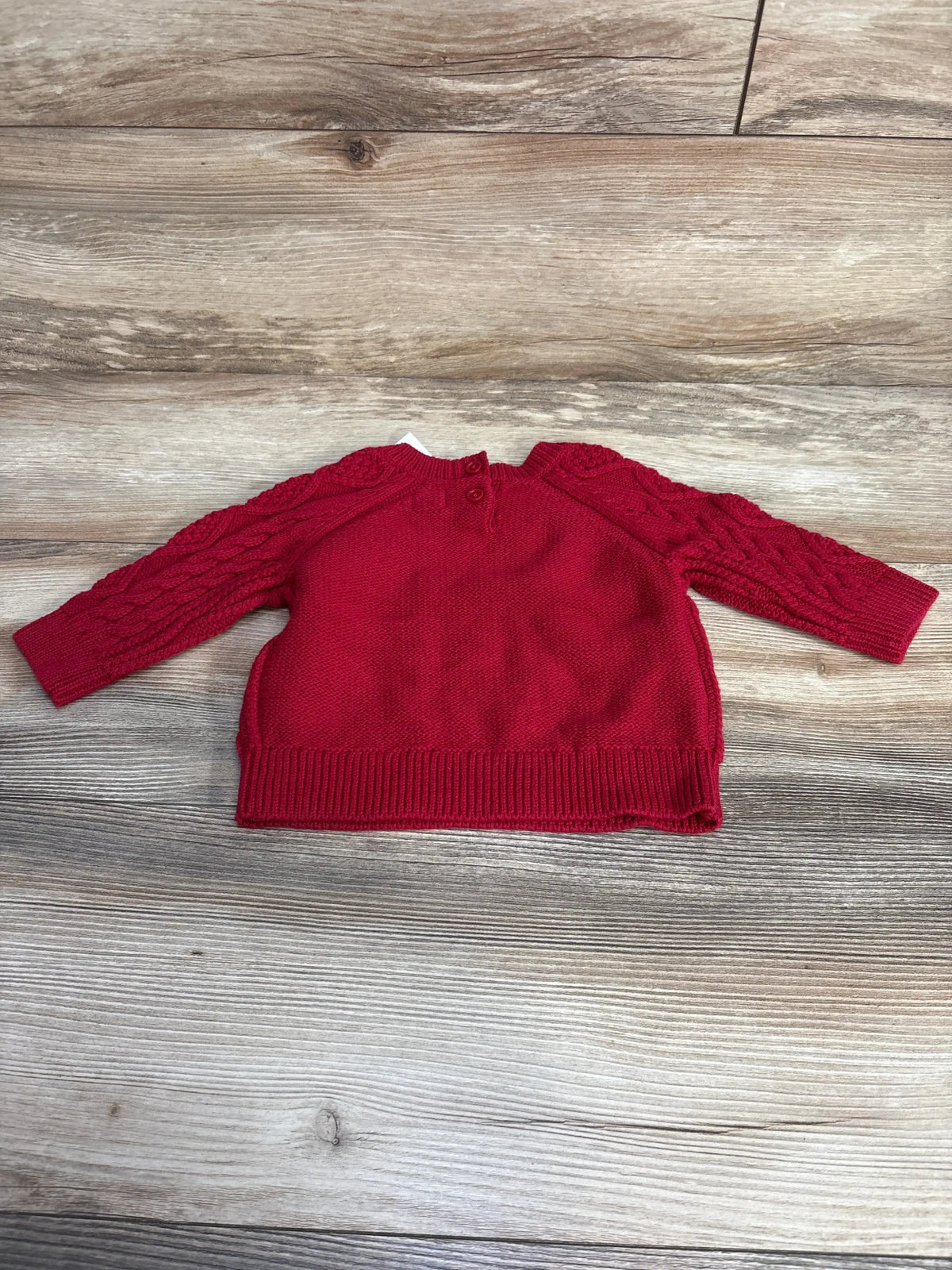 Flat lay of Baby Gap red cable knit baby sweater size 3-6 months showing cable-knit sleeves and button-back neck on wood background