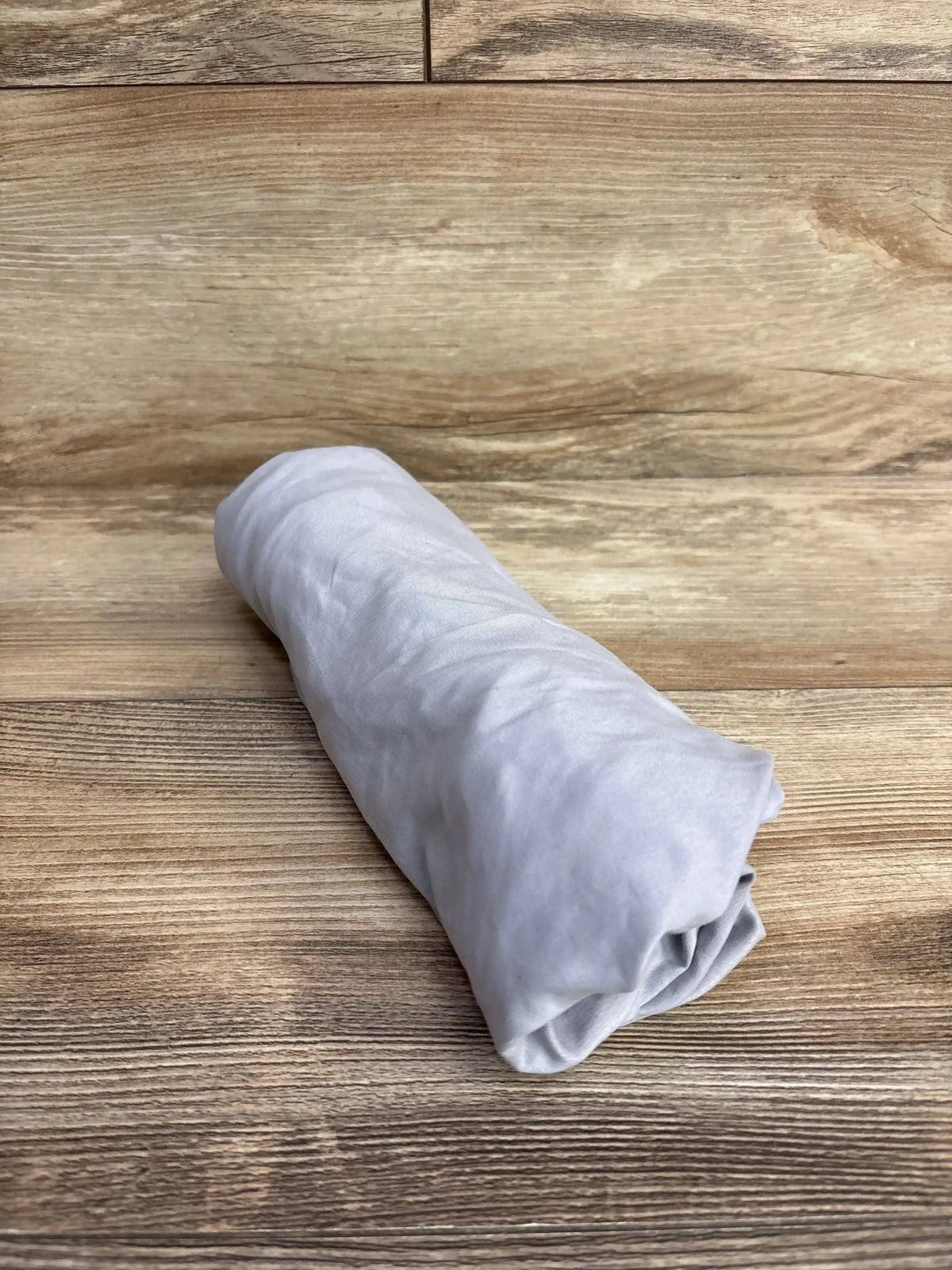 Rolled view of Parent’s Choice fitted bassinet sheet in grey showcasing soft lightweight fabric on wooden surface