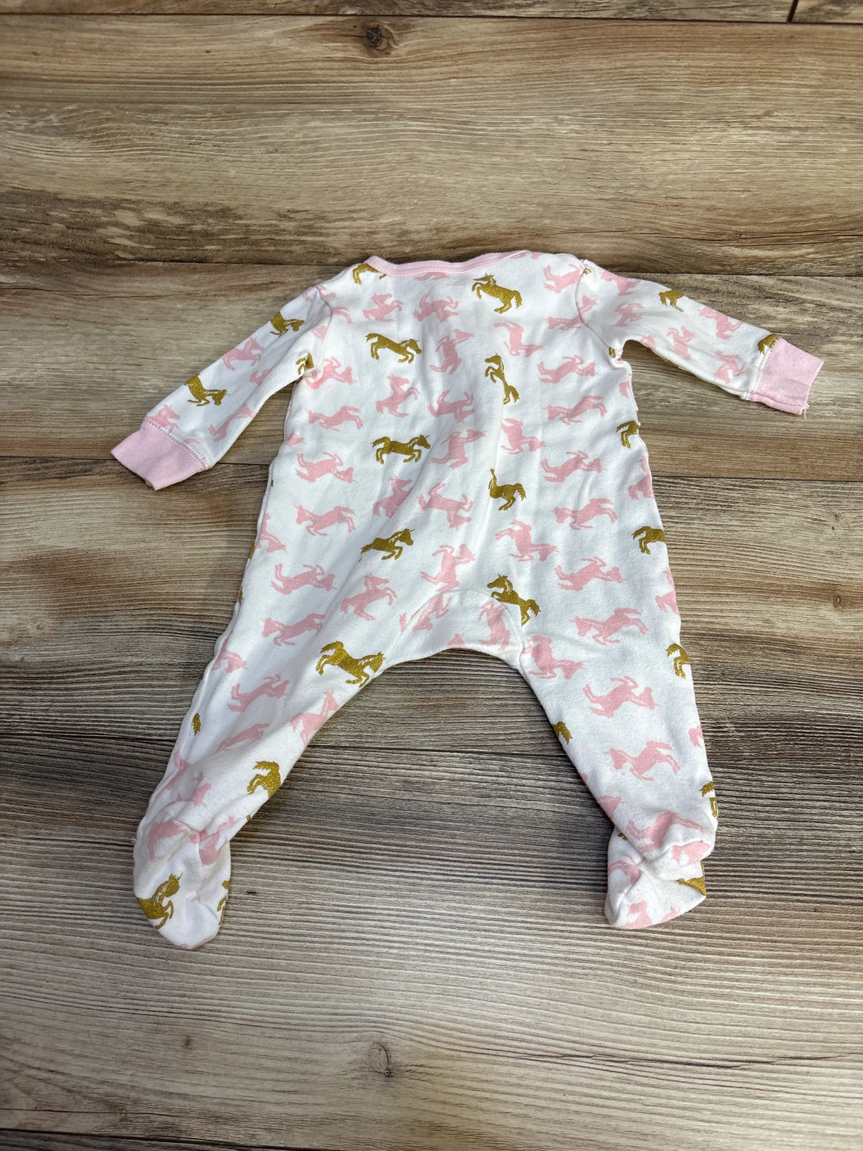 Baby sleeper with pink and gold unicorn print on wooden background