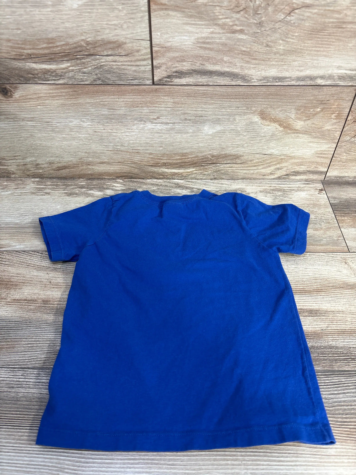 Back view of Port & Company toddler shirt in blue, size 4T, showcasing the crew neck and relaxed fit on a wood-look floor