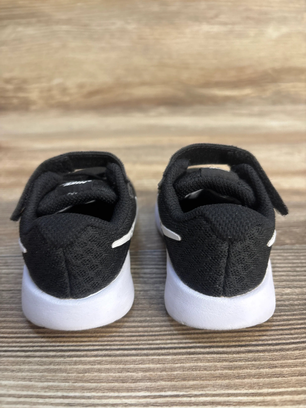 Black toddler sneakers with white soles on wood background, gently used kids shoes