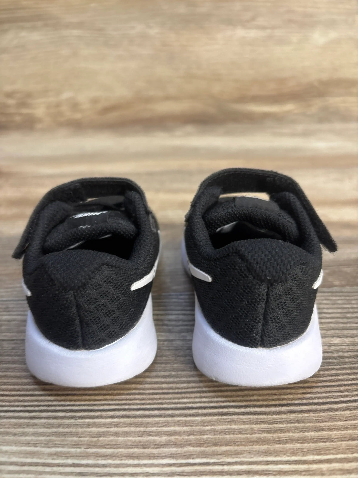 Black toddler sneakers with white soles on wood background, gently used kids shoes