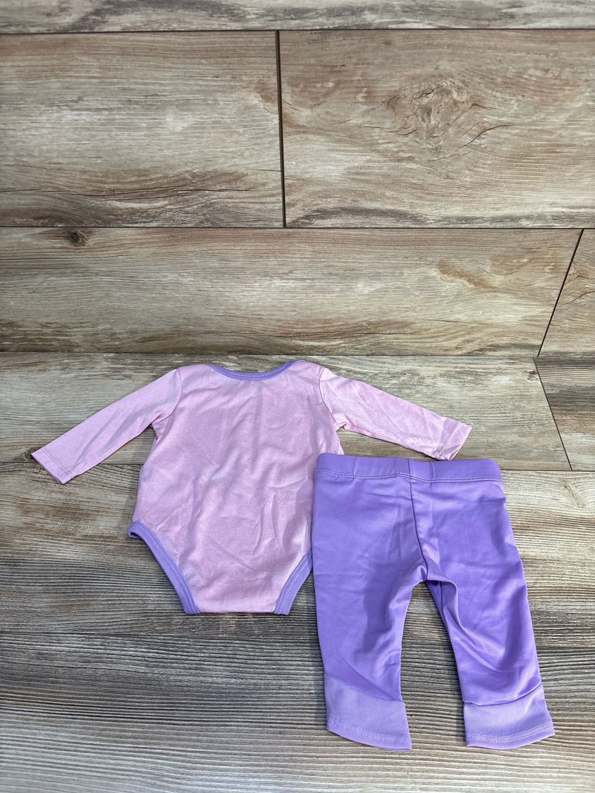 Front view of Nike two-piece bodysuit and pants set showcasing a pink long-sleeve bodysuit and matching pants on a wood surface