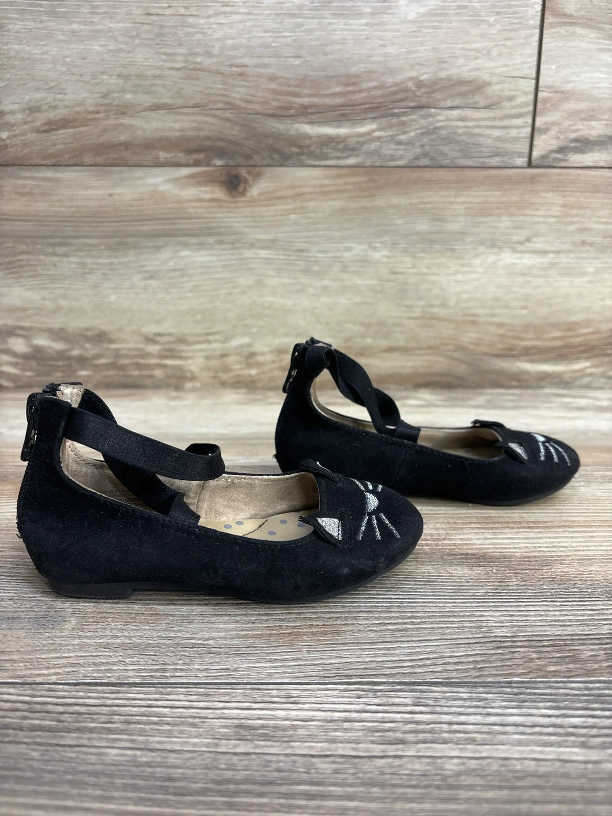 Black toddler girl shoes with cat face embroidery and ankle straps on wood floor background
