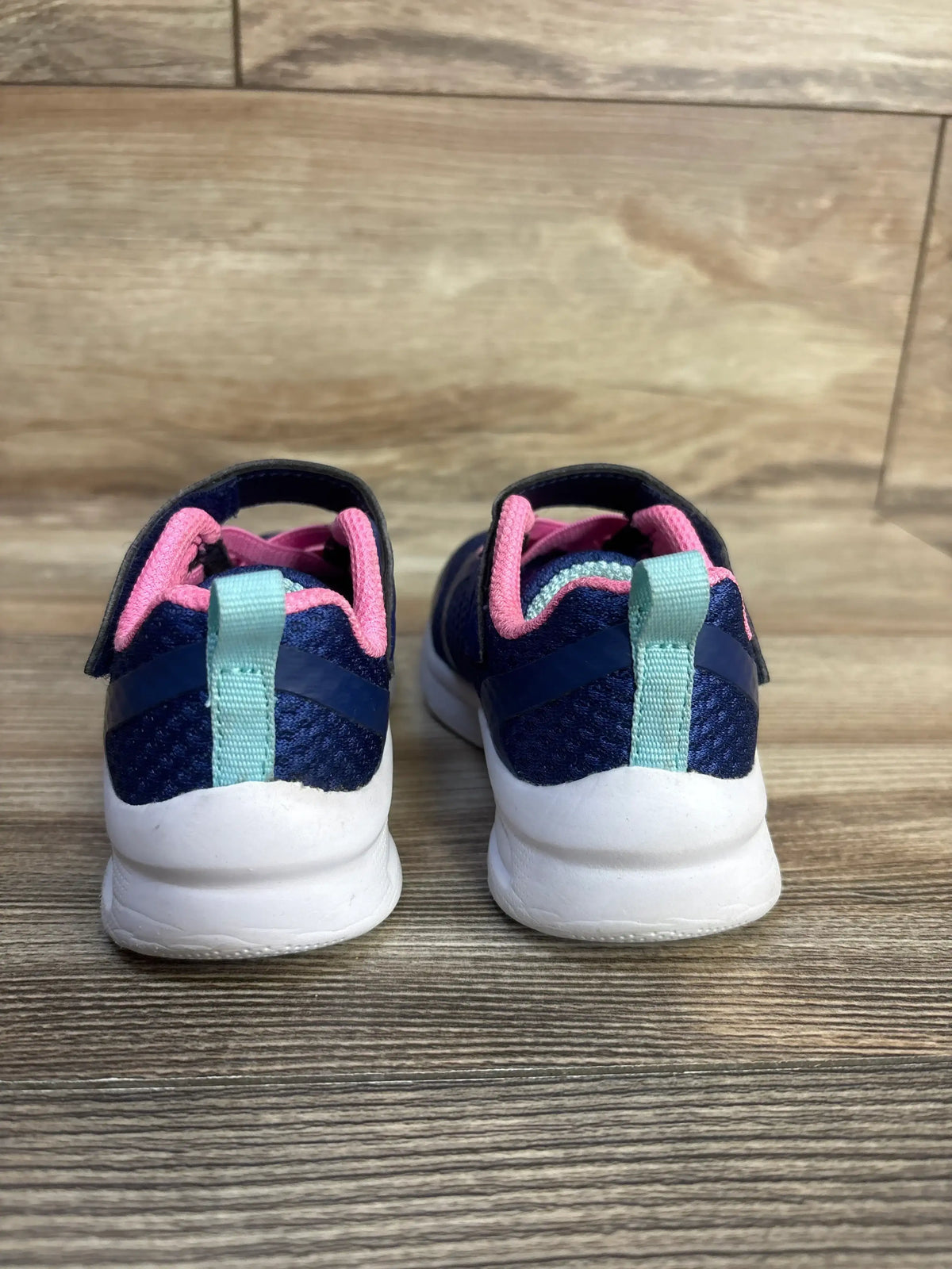 Rear view of Skechers toddler sneakers in navy showing mint heel tab, pink lining, velcro strap and white sole on wood floor
