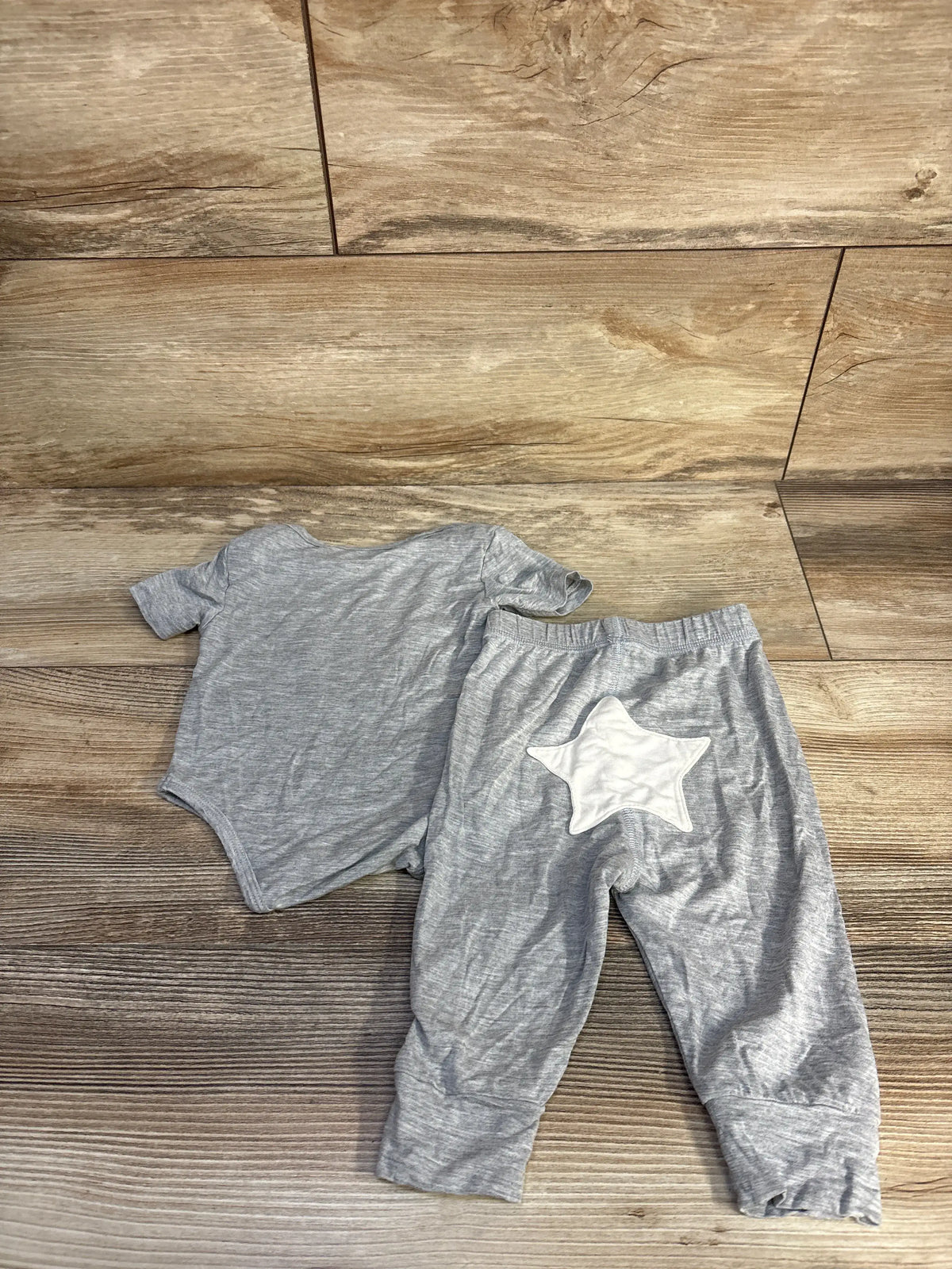 Front view of Earth Baby grey bamboo bodysuit and pants set showcasing a white star patch on a wood floor