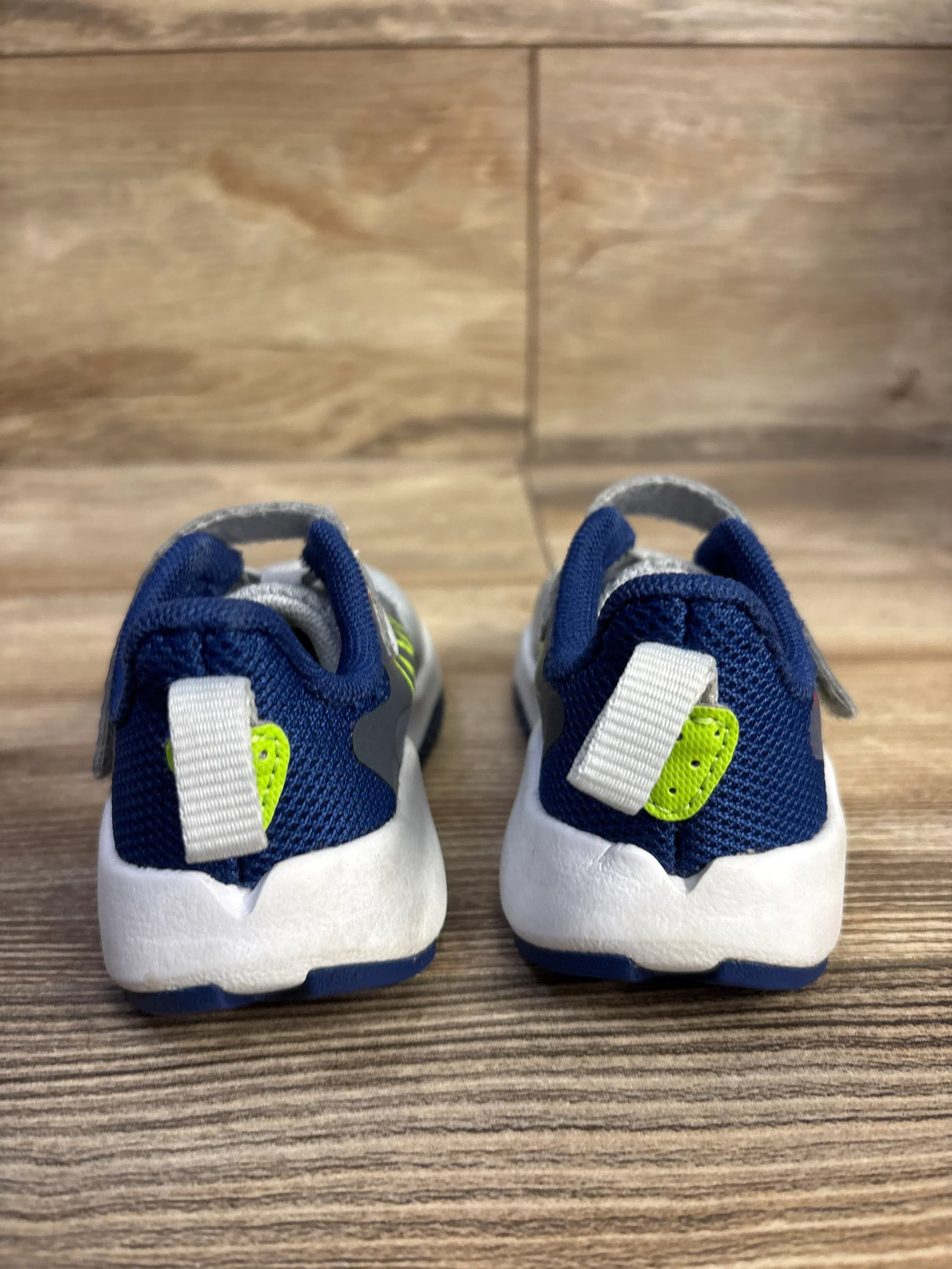 Back view of blue and white toddler sneakers with neon green heart detail on wood floor