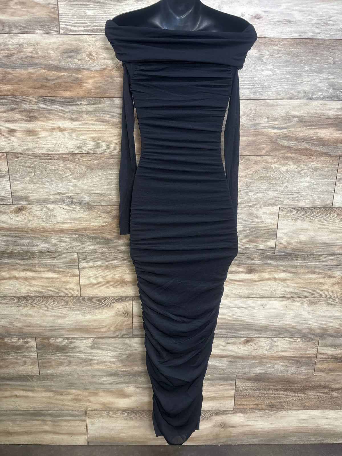 Front view of Bumpsuit black ruched mesh dress showcasing an off-the-shoulder neckline and maxi length on a wood floor