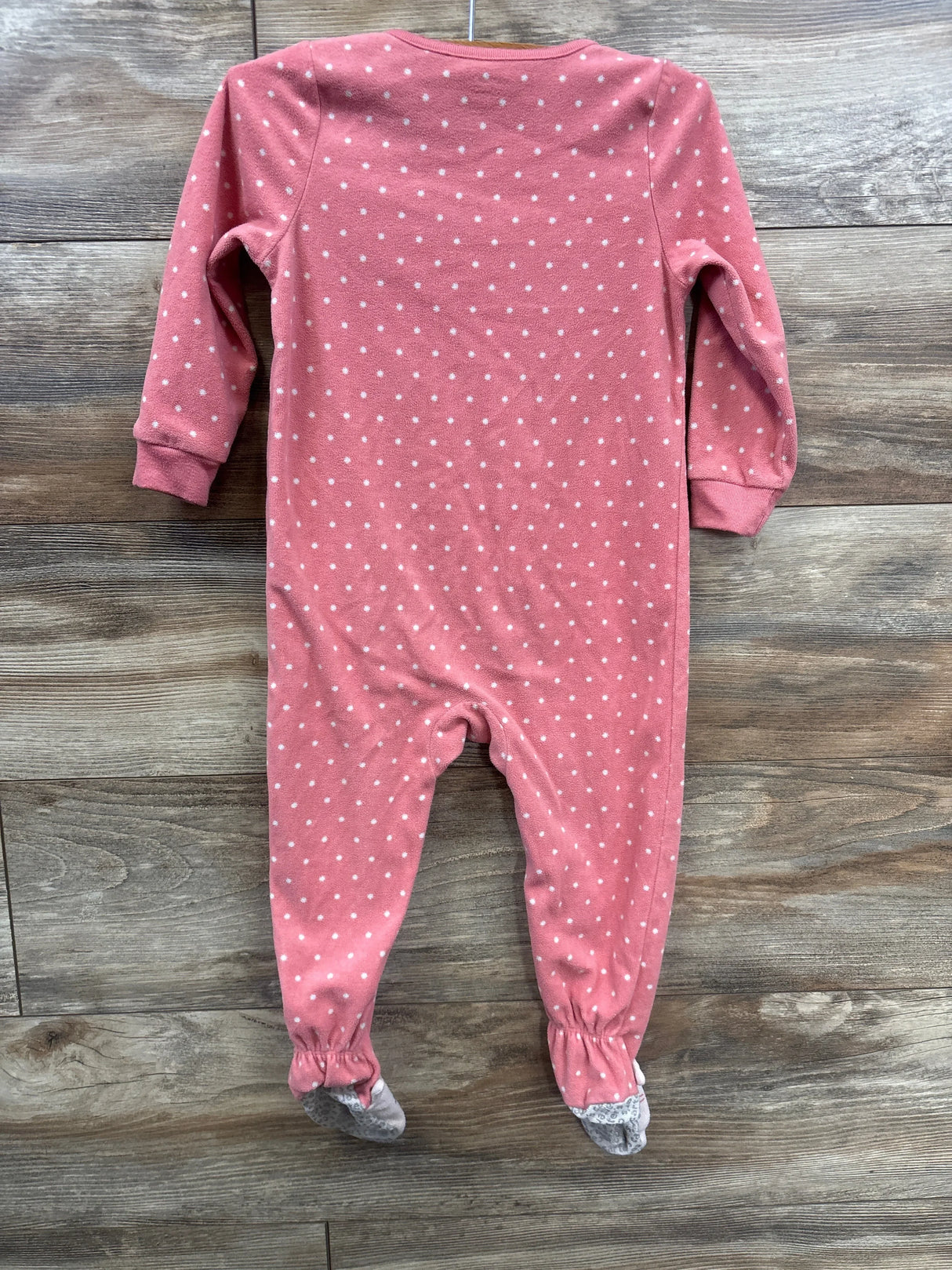 Pink baby footed sleeper with white polka dots, long sleeves, on wood floor