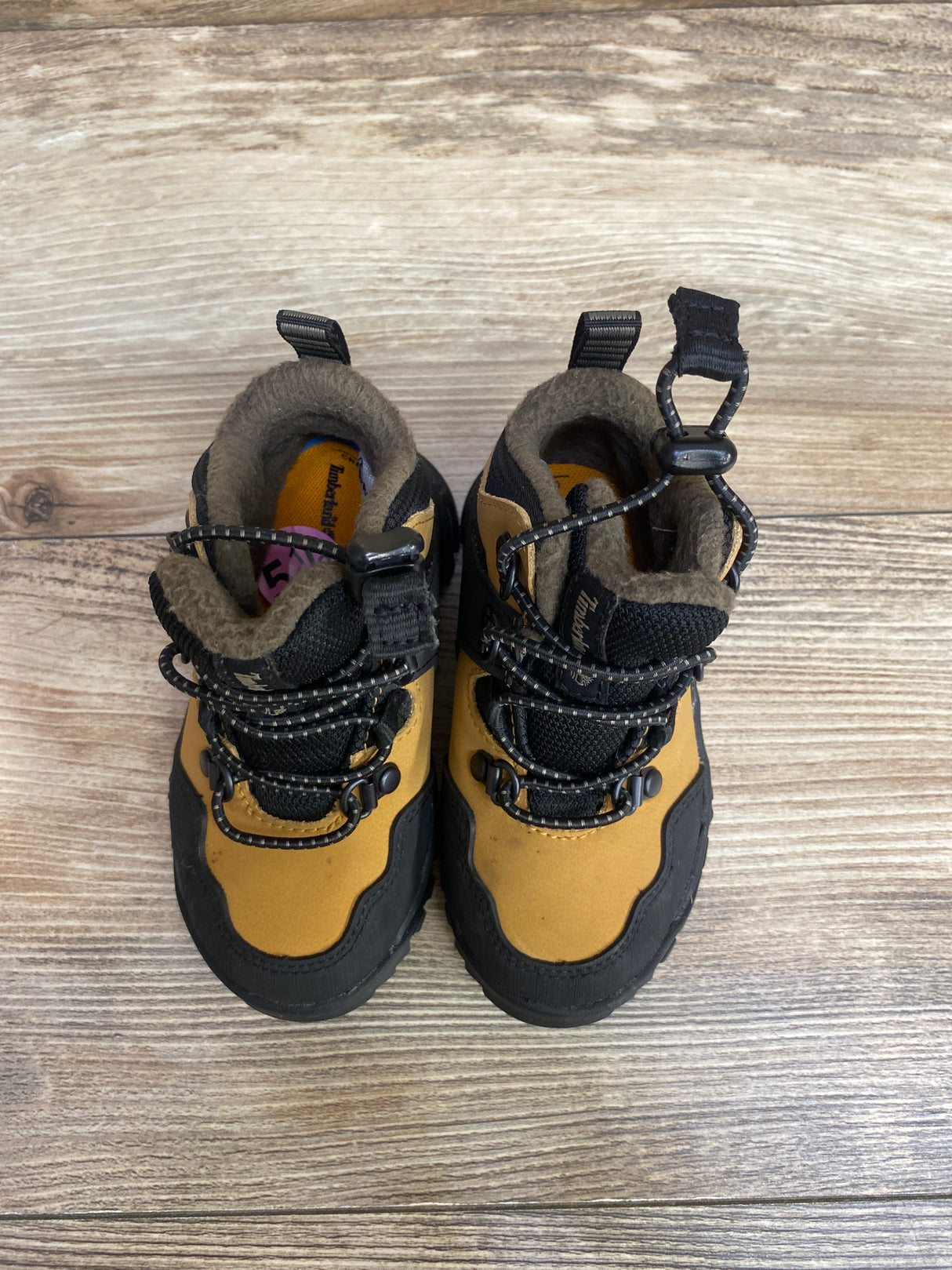 Top view of toddler Timberland boots with black and tan design on wooden floor