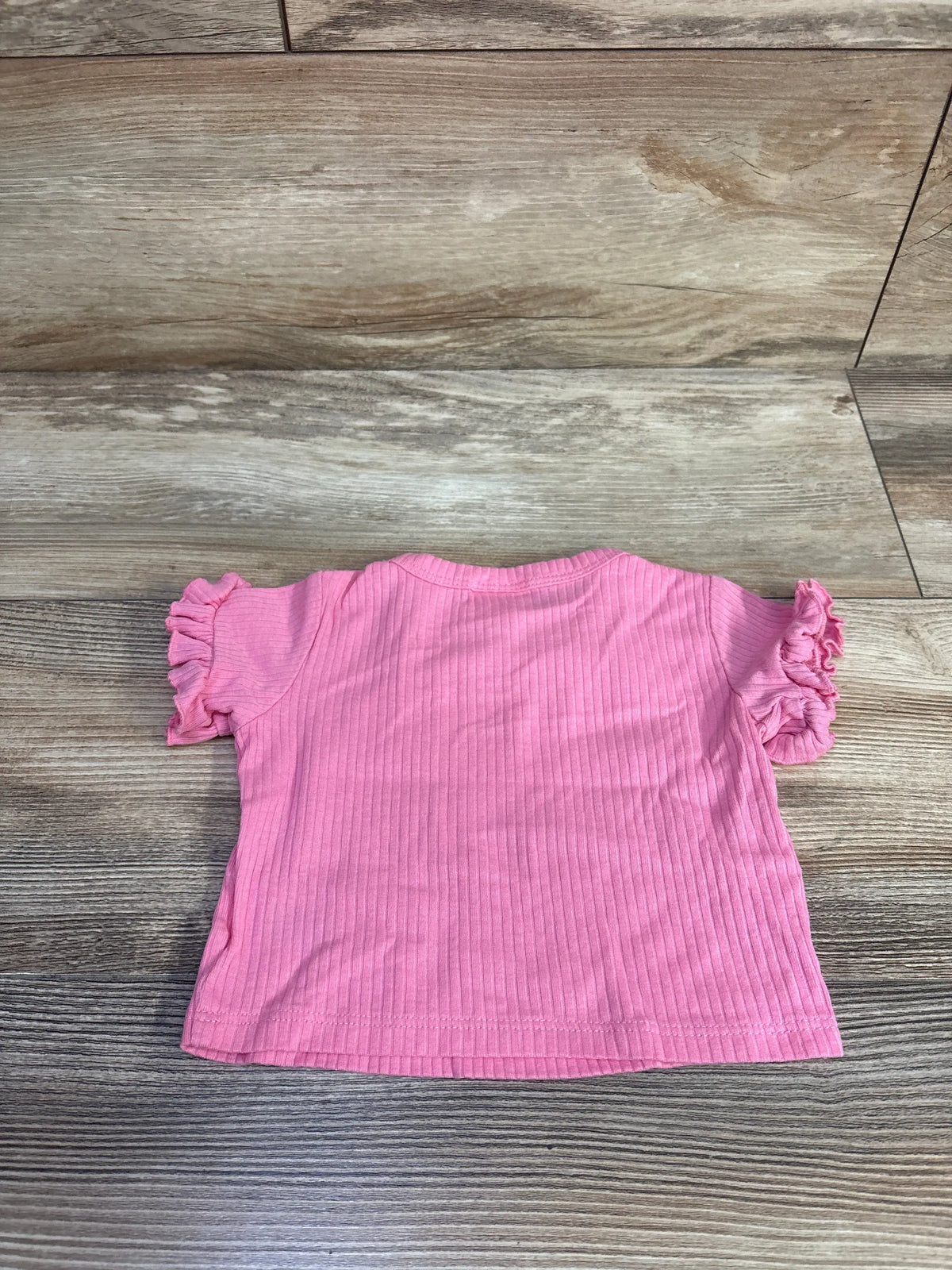 Front view of Cat & Jack ribbed shirt showcasing pink ribbed fabric and ruffled short sleeves on a wood-grain background