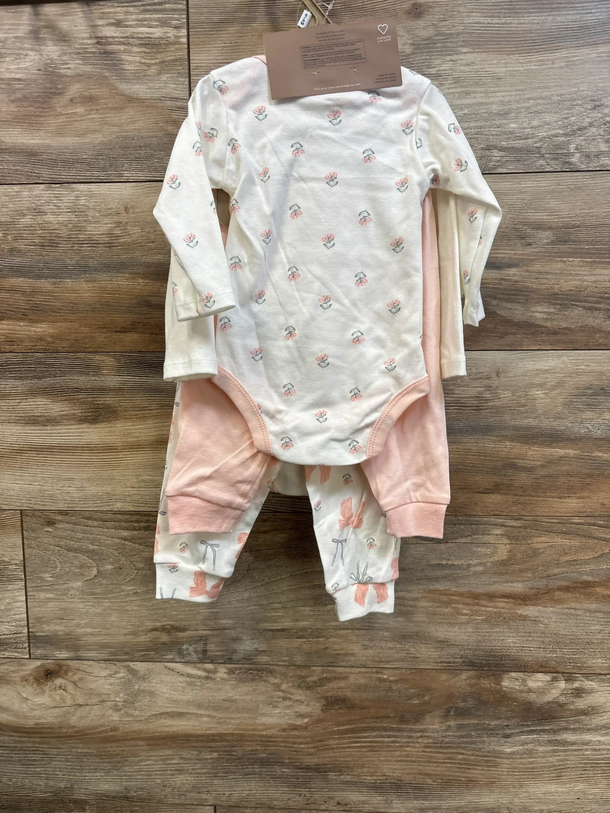 Top-down view of a white five-piece baby bodysuit set with pink accents and floral prints on a wood surface