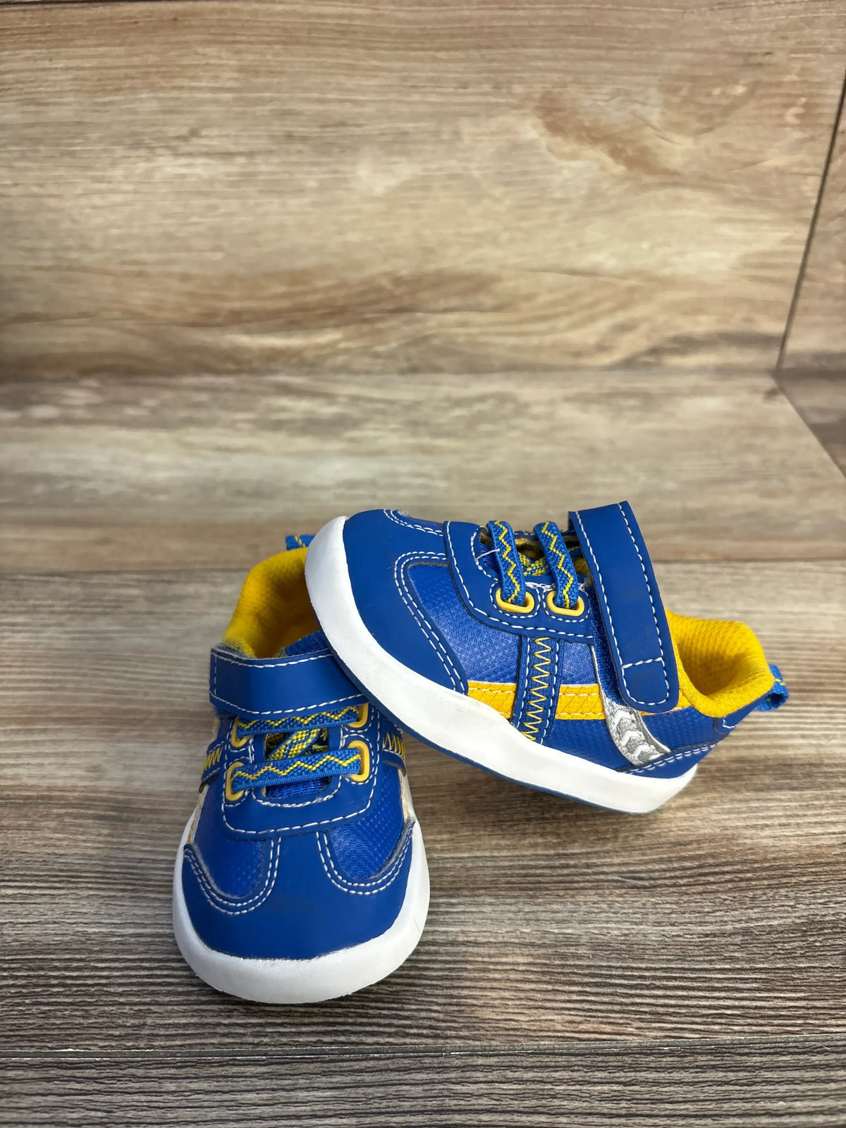 Side view of blue Wonder Nation sneakers, size 3C, showcasing Velcro straps, yellow accents, and white soles on a wood-grain floor